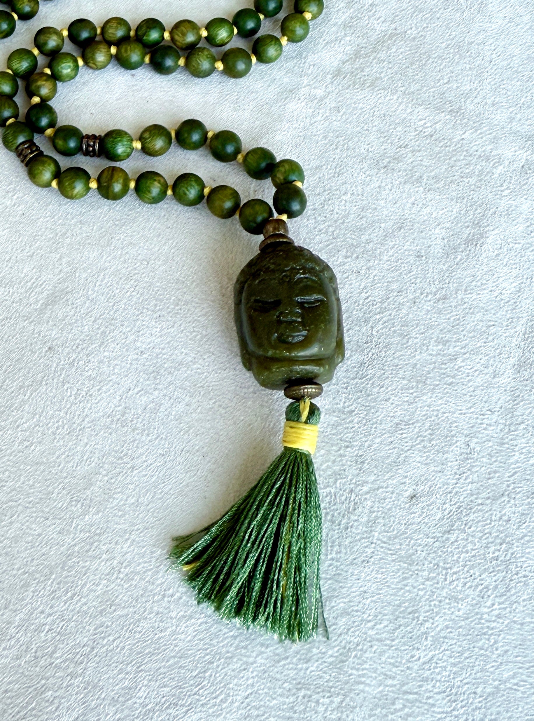 Close-up of Buddha Jade pendant on a natural sandalwood mala beads showing smooth texture and warm brown tones