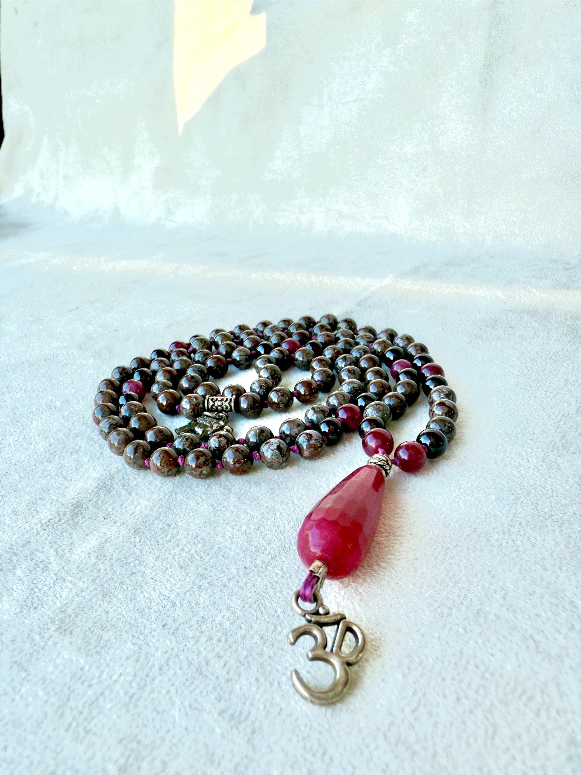Close-up of om charm 6mm beads: grey-flecked obsidian next to deep red garnet, knots visible,