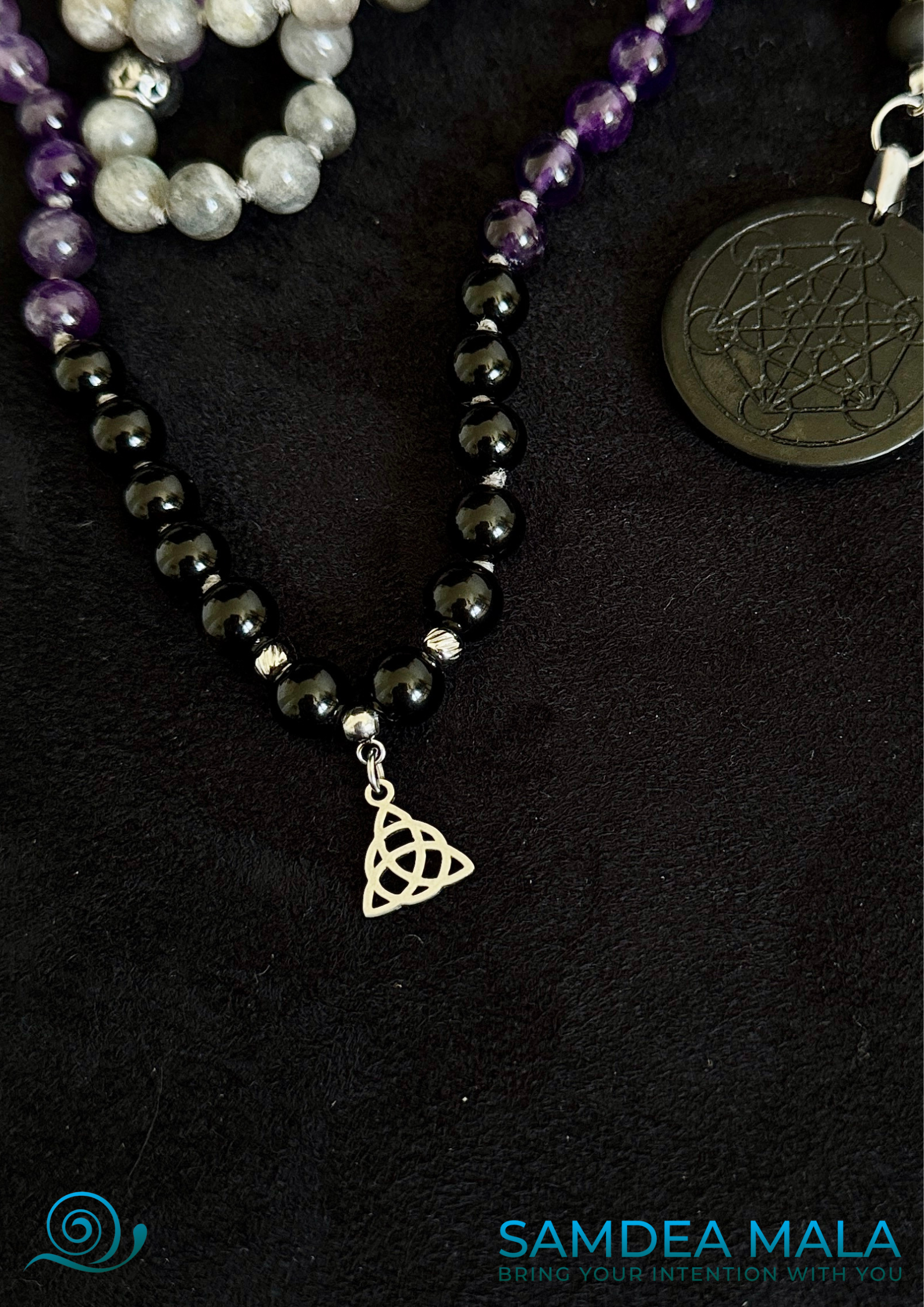 Close up of Small Triquetra pendant – an ancient symbol of life cycles and the unity of body, mind, and soul. Samdea Mala for shadow work with obsidian, amethyst, and labradorite, hand knotted mala, handmade in US. 108 grounding meditation beads with dark feminine spiritual energy. Inner child and trauma healing mala. Metatron’s Cube pendant in shungite and sacred symbols.