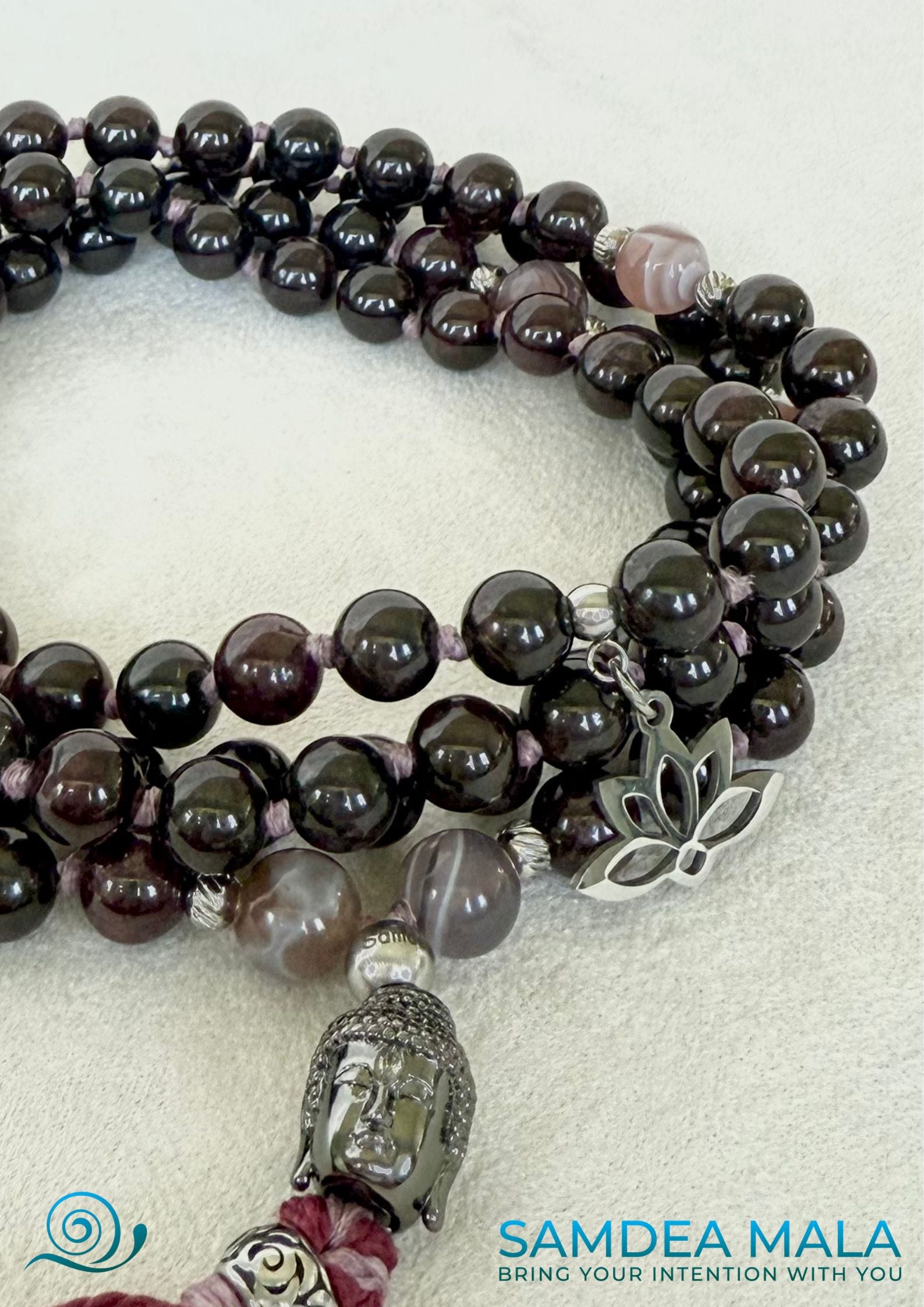 Close up of 108 prayer beads for a spiritual gift. Custom mala in granet and Botwane Agate with tassel; purple, bordeaux mala beads with Buddha and lotus charm, for protection and light.