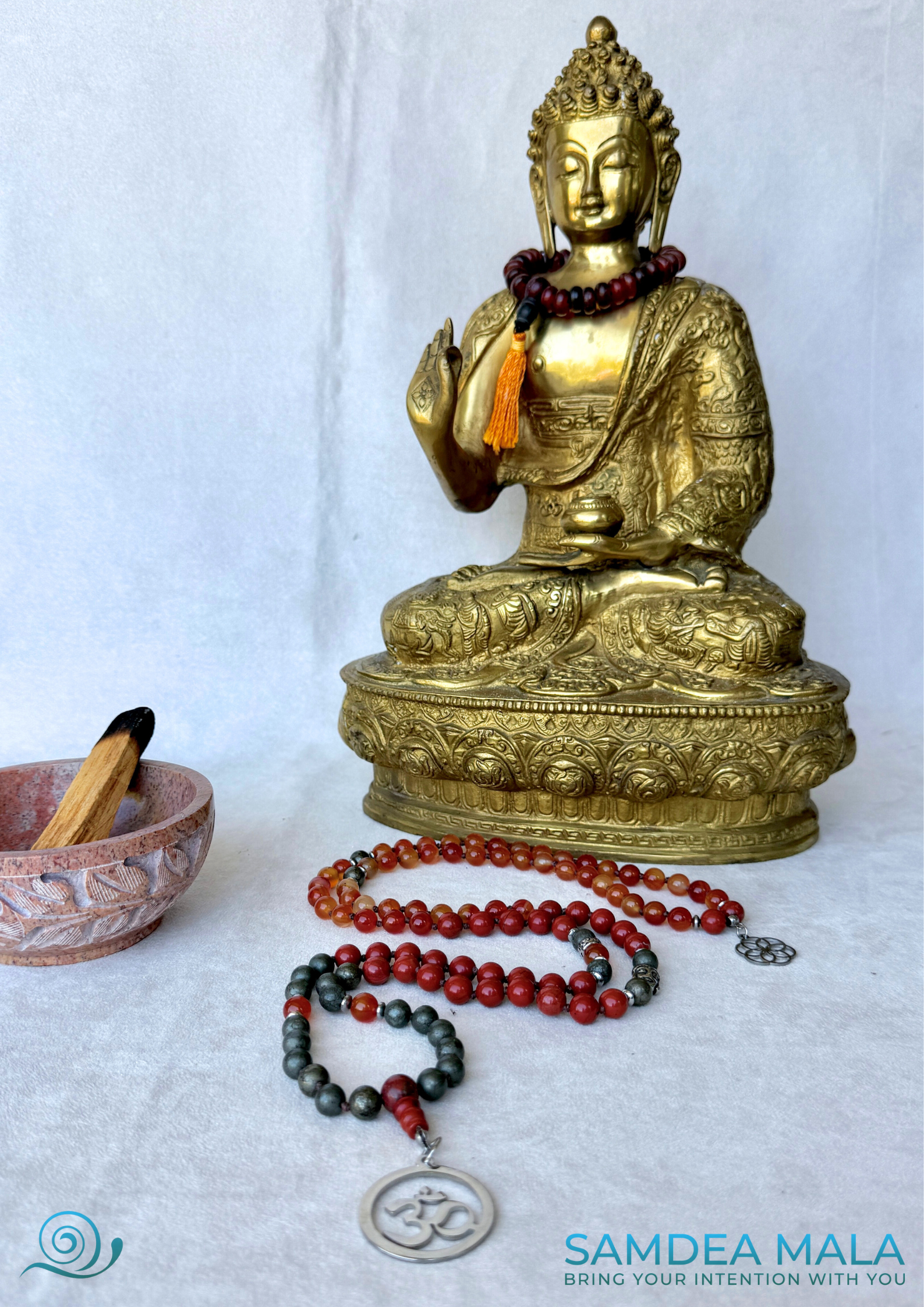 Grounding mala beads with Om pendant, Buddha charm and seed of life small pendant. Natural stones – Red Jasper, Carnelian, Pyrite. Zodiac sign Aries Mala for meditation. A buddha statue on the scene,
