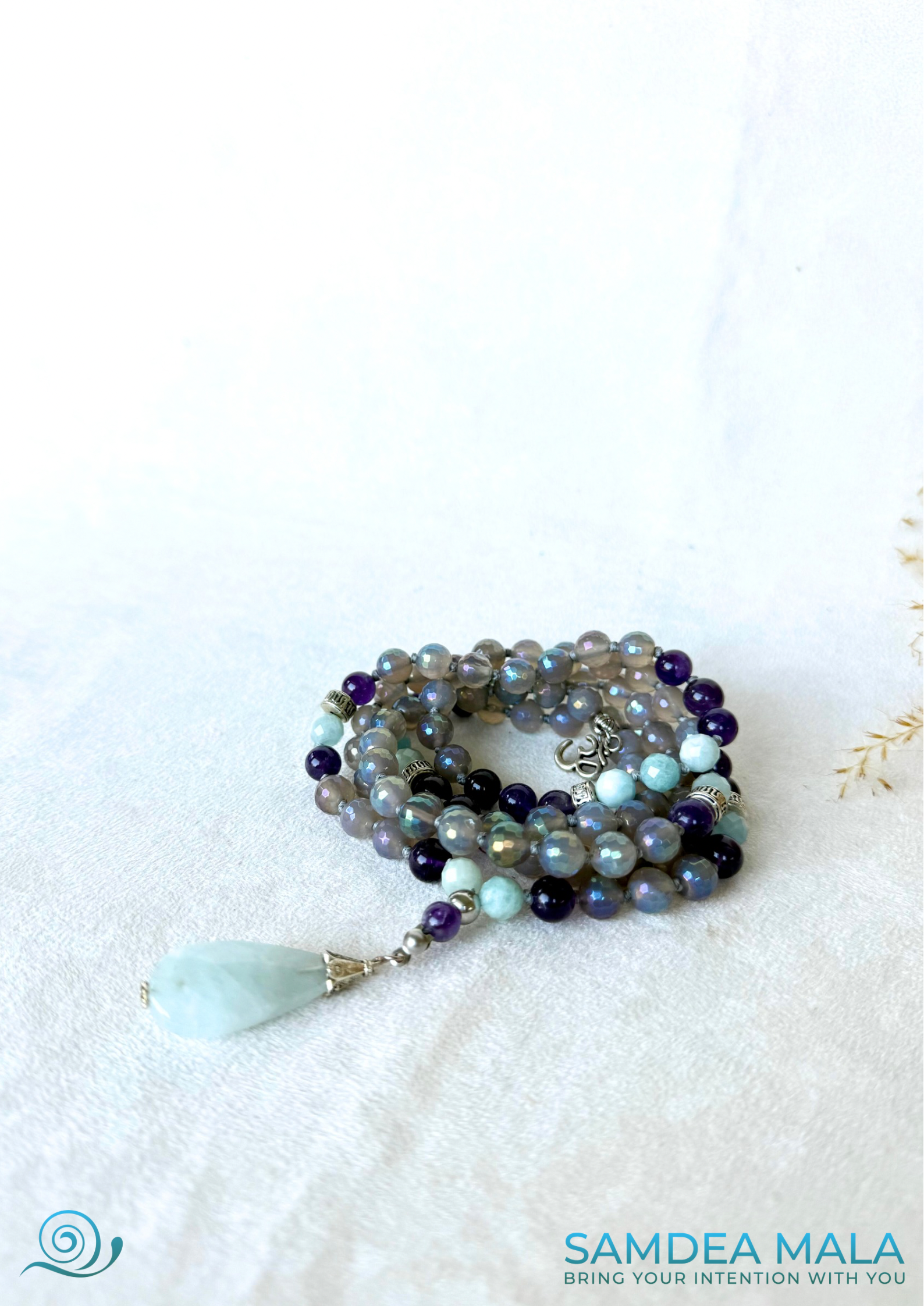108 spiritual beads and OM charm by Samdea Mala, with gray agate, amethyst, and aquamarine beads. Hand-knotted mala necklace with natural aquamarine pendant.