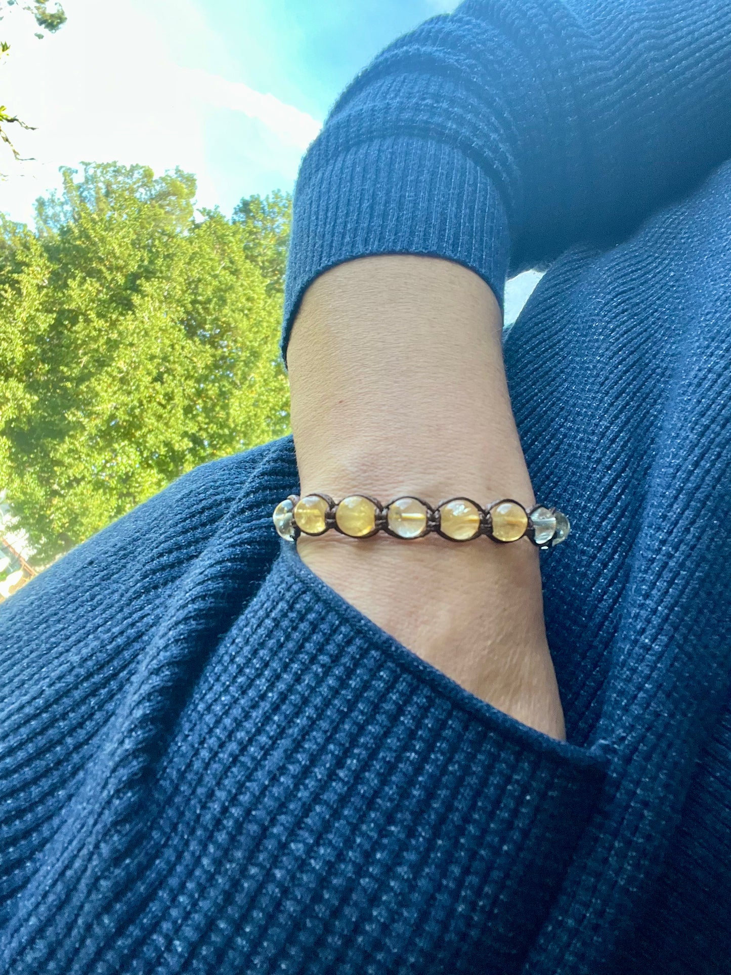 A bracelet featuring translucent yellow and clear round beads on brown cord. The bracelet is handcrafted with natural stones and is approximately 7 inches in length.  It's a stylish and unique piece of jewelry perfect for adding a touch of elegance to any outfit.