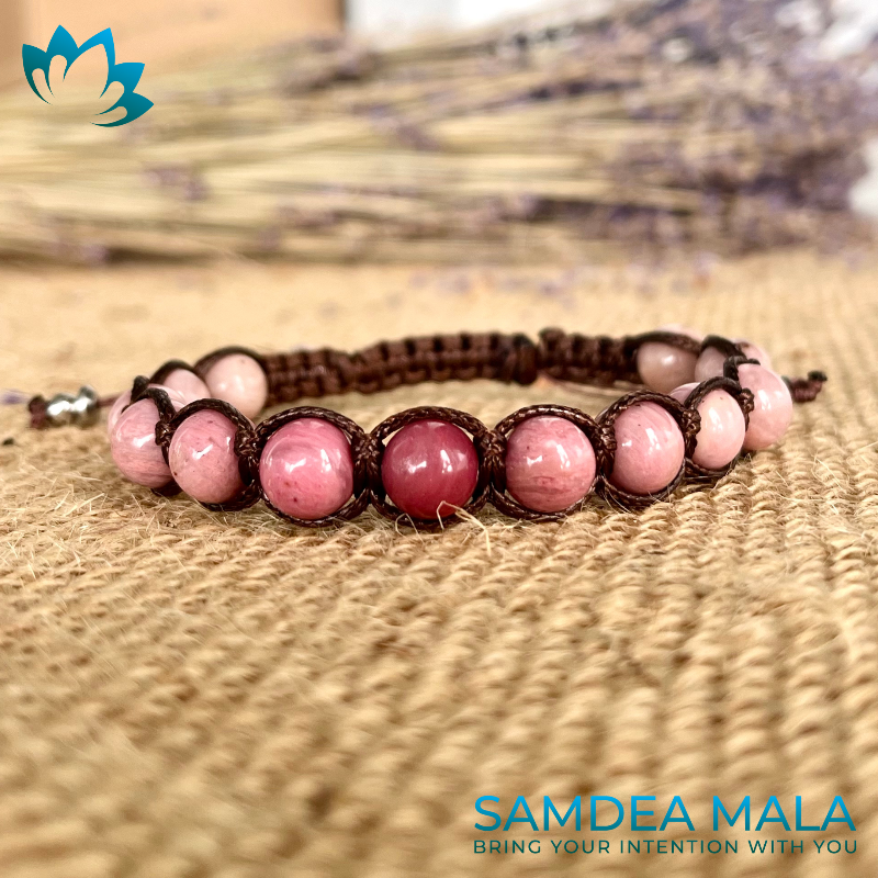 Close-up of a pink rhodonite gemstone mala bracelet with brown cord. The bracelet features round, polished pink rhodonite beads interspersed with smaller brown spacer beads. For love, compassion, Purpose & Collective Harmony