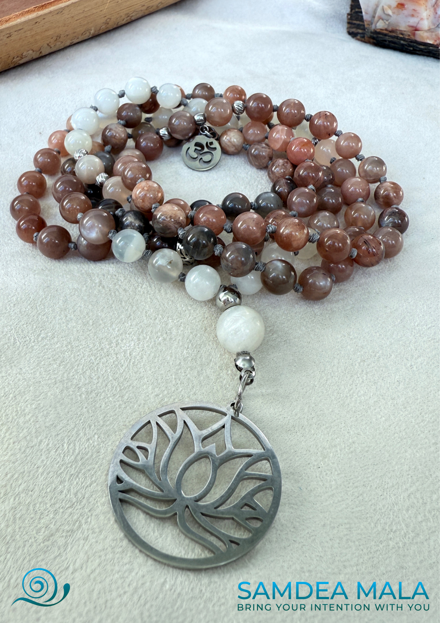 Moonstone Mala with Buddha, Lotus and OM – Hand-Knotted Feminine Energy Mala | Intuition Mala with Lotus Pendant | 108 Beads | Self-Connection & Lunar Magic. Hand knotted, handcrafted in US. 108 moonstone beads in soft pink and gray hues, Spiritual jewelry for intuition, lunar energy, and inner self-connection. Moonstone mala necklace.