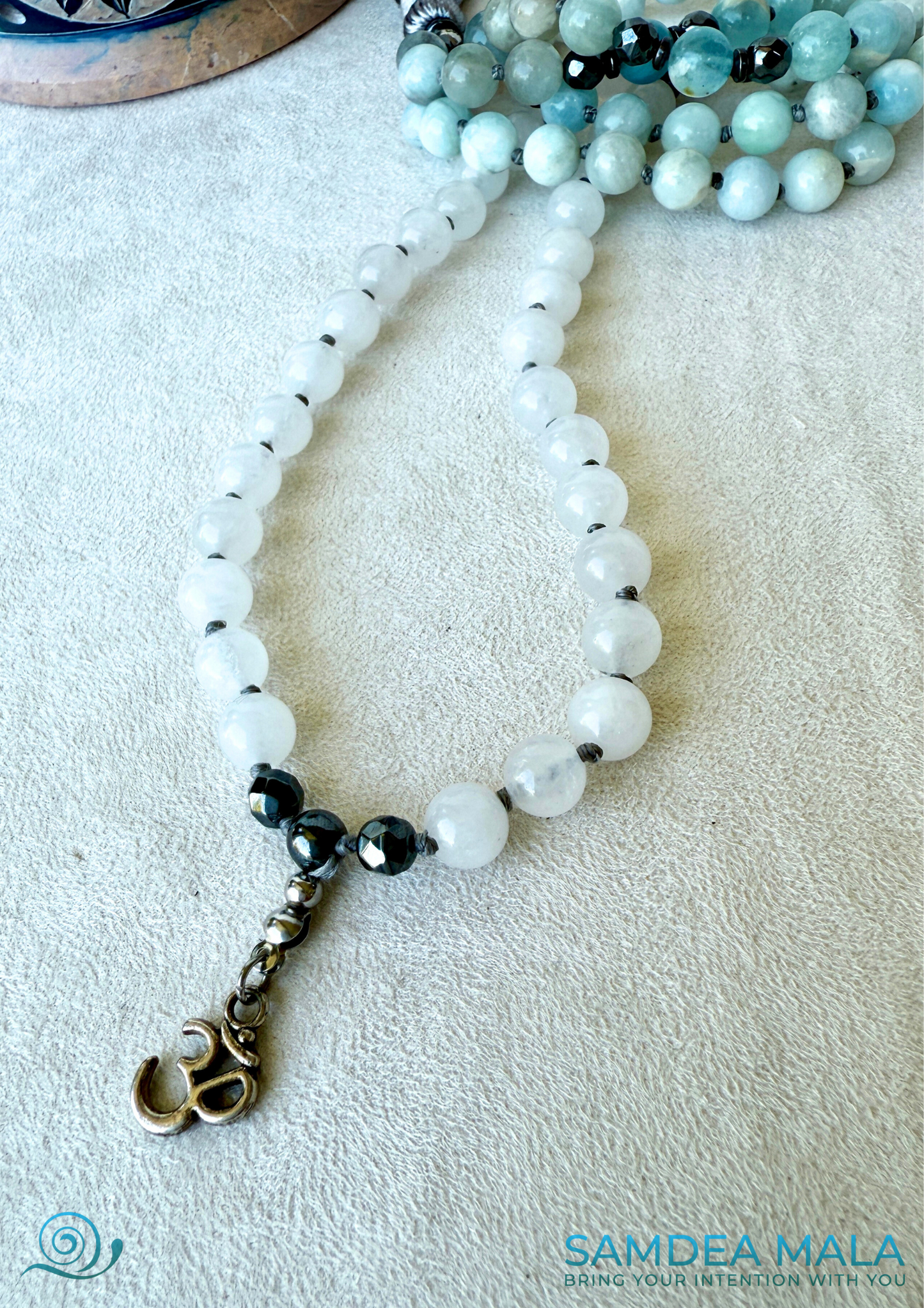 Detail of mala beads in soft blue Aquamarine and white jade tones for mindful living - om charm