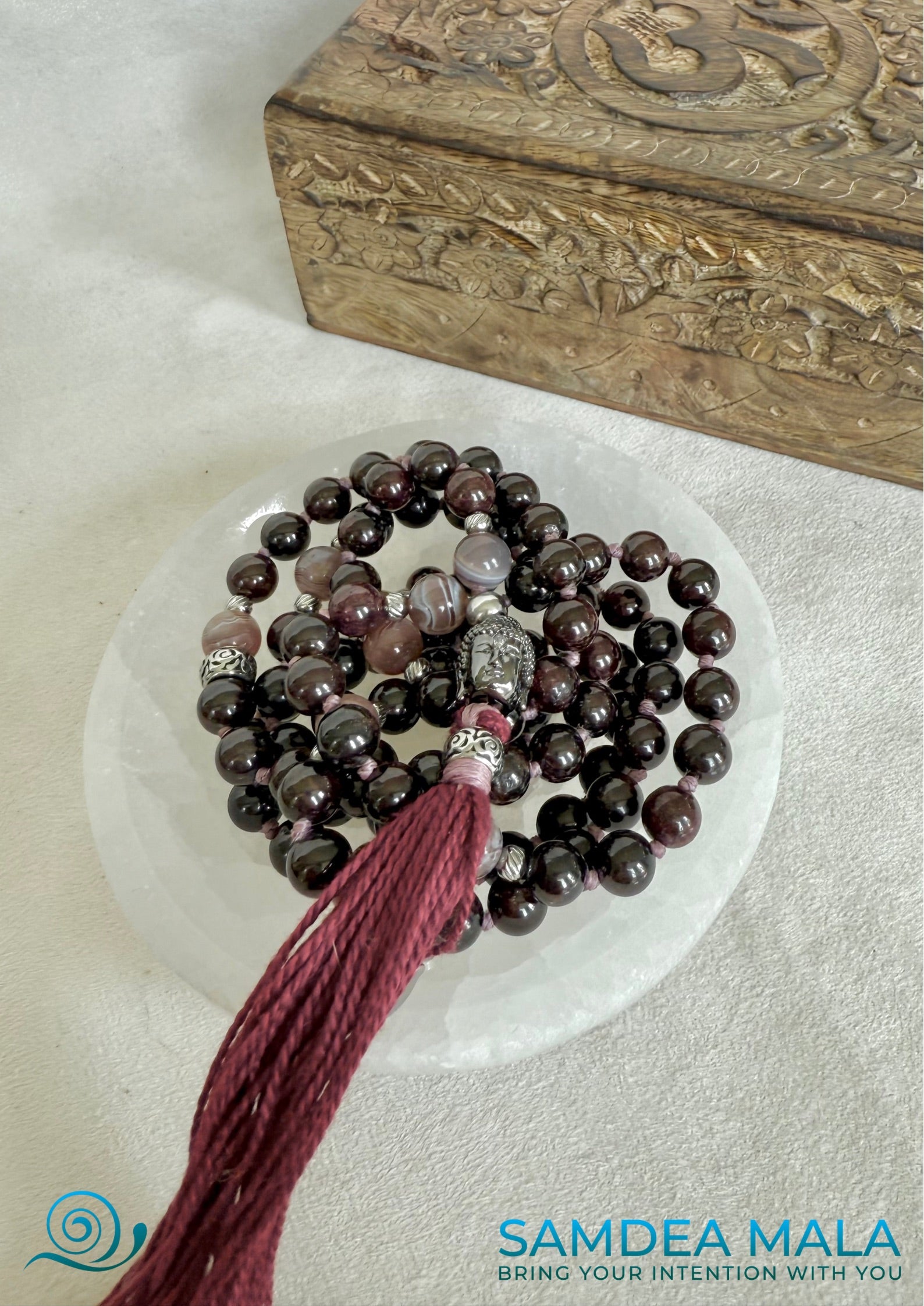 Custom mala with tassel on a selenite bowl, mala beads with Buddha and lotus charm, for protection and light. Garnet and botwane agate hand knotted mala for meditation.