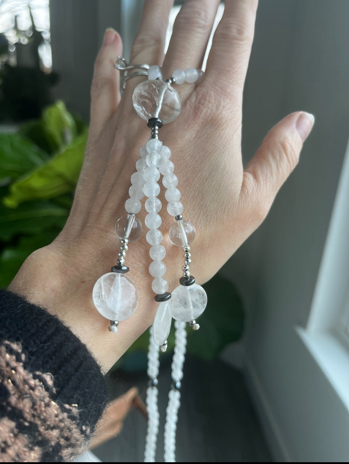 A hand holding a White Juzu - Nichiren Buddhist Prayer Beads - natural spiritual white gemstones: White jade, clear quartz, steel and ematite.