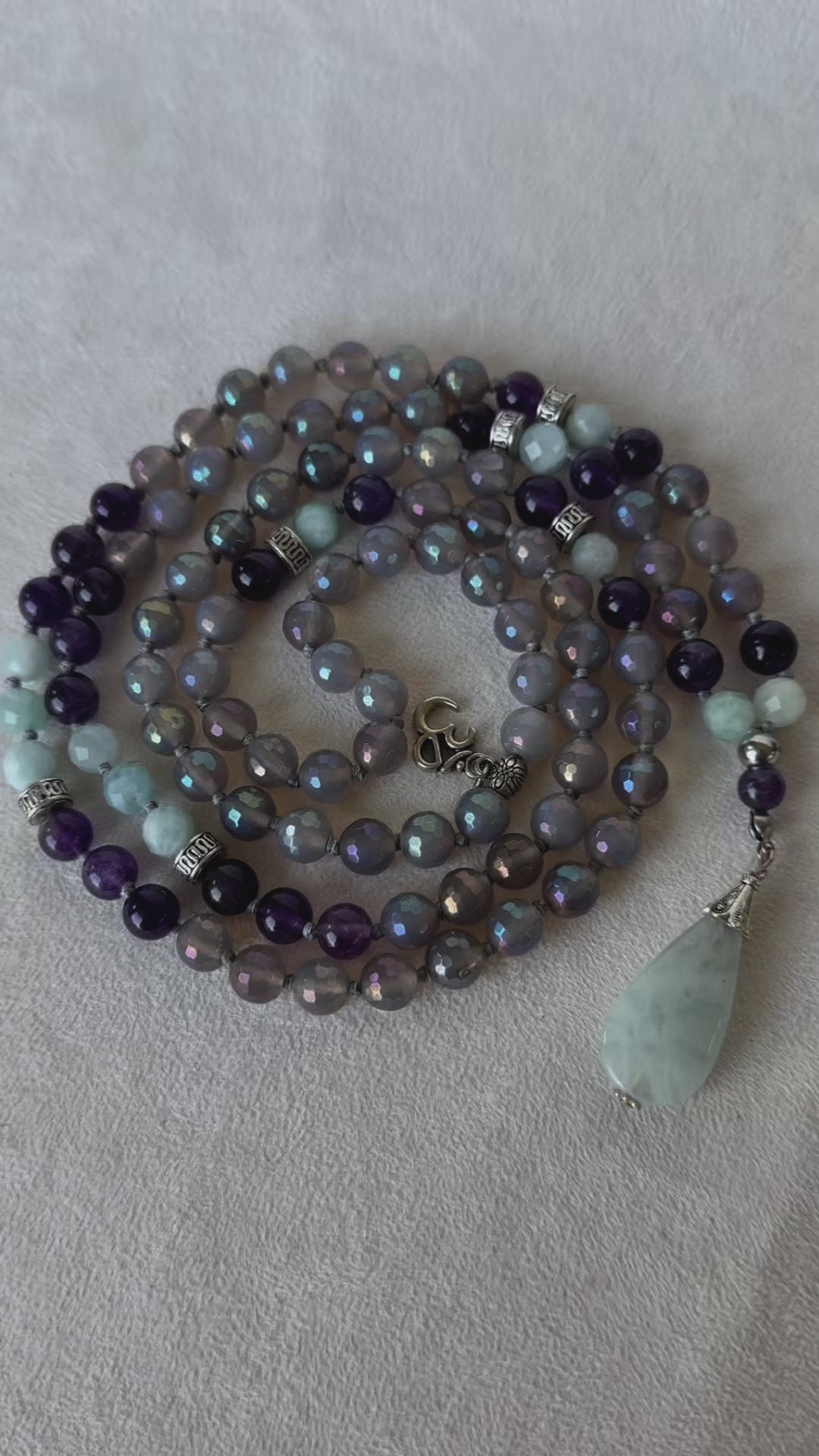 108 spiritual beads and OM charm by Samdea Mala, with gray agate, amethyst, and aquamarine beads. Hand-knotted mala necklace with natural aquamarine pendant.