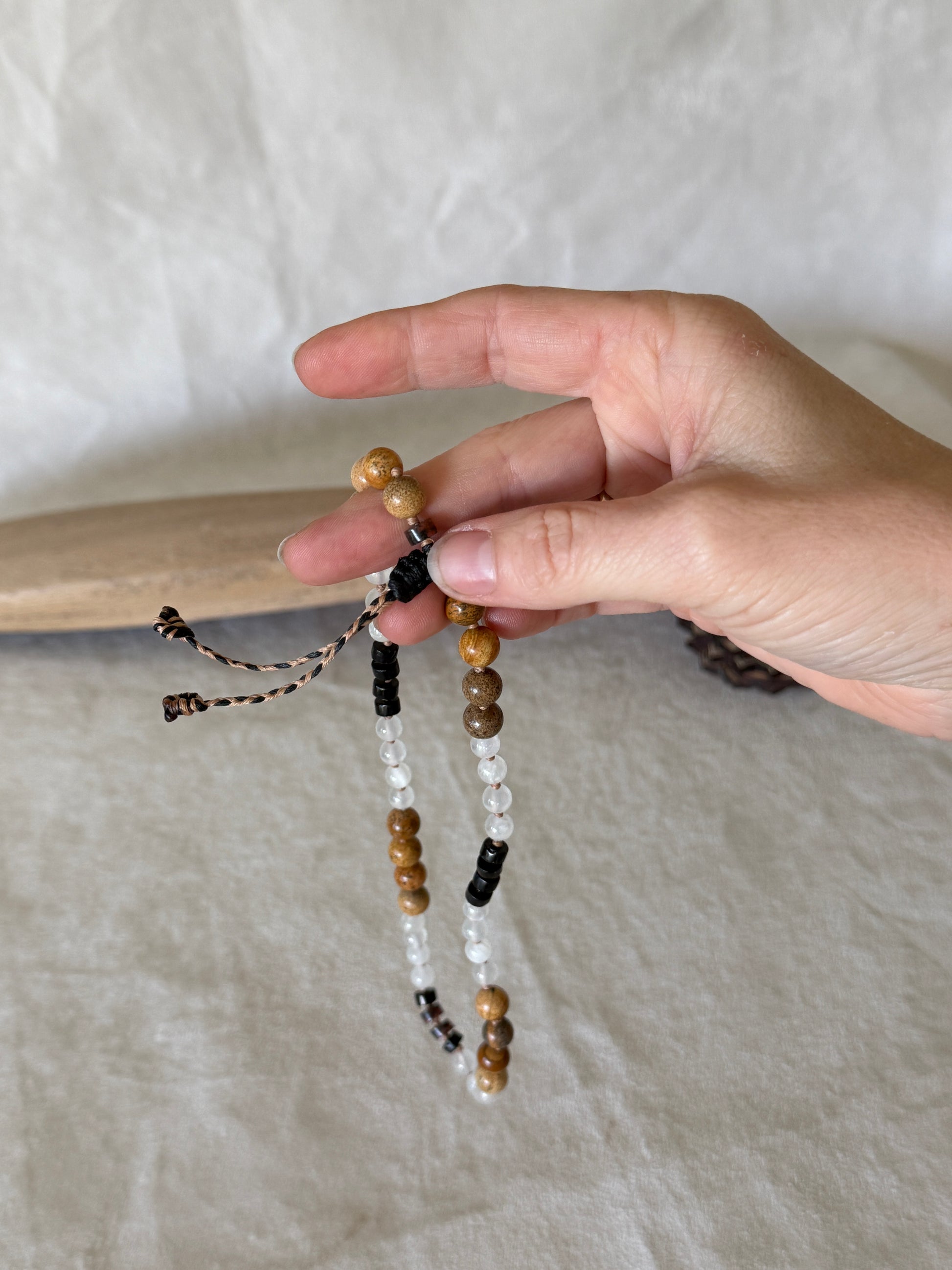 A hand holding  a grounding natural gemstone obosidian, selenite, jasper breathing mala bracelet with groups of four beads to guide inhale, hold, exhale, and hold during breathwork practice. 