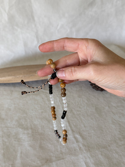 A hand holding  a grounding natural gemstone obosidian, selenite, jasper breathing mala bracelet with groups of four beads to guide inhale, hold, exhale, and hold during breathwork practice. 