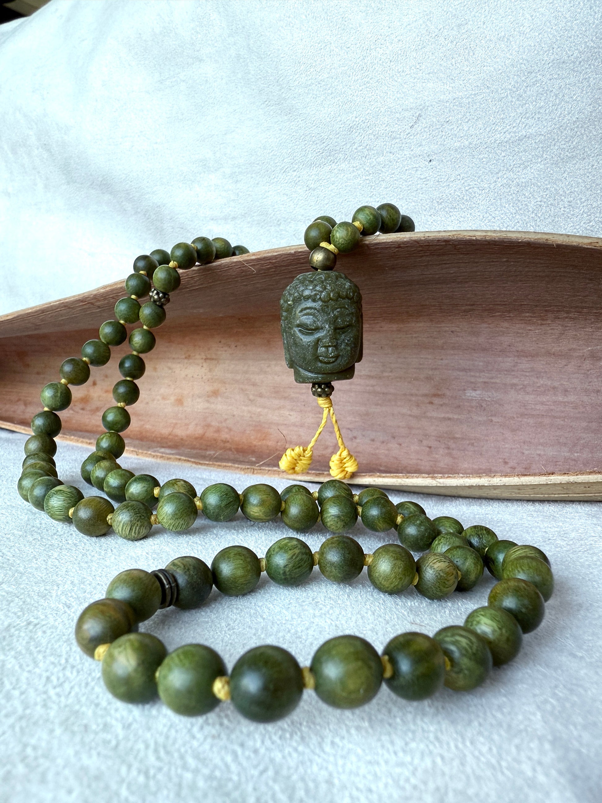 Close-up of Buddha Jade pendant on a natural sandalwood mala beads showing smooth texture and warm brown tones