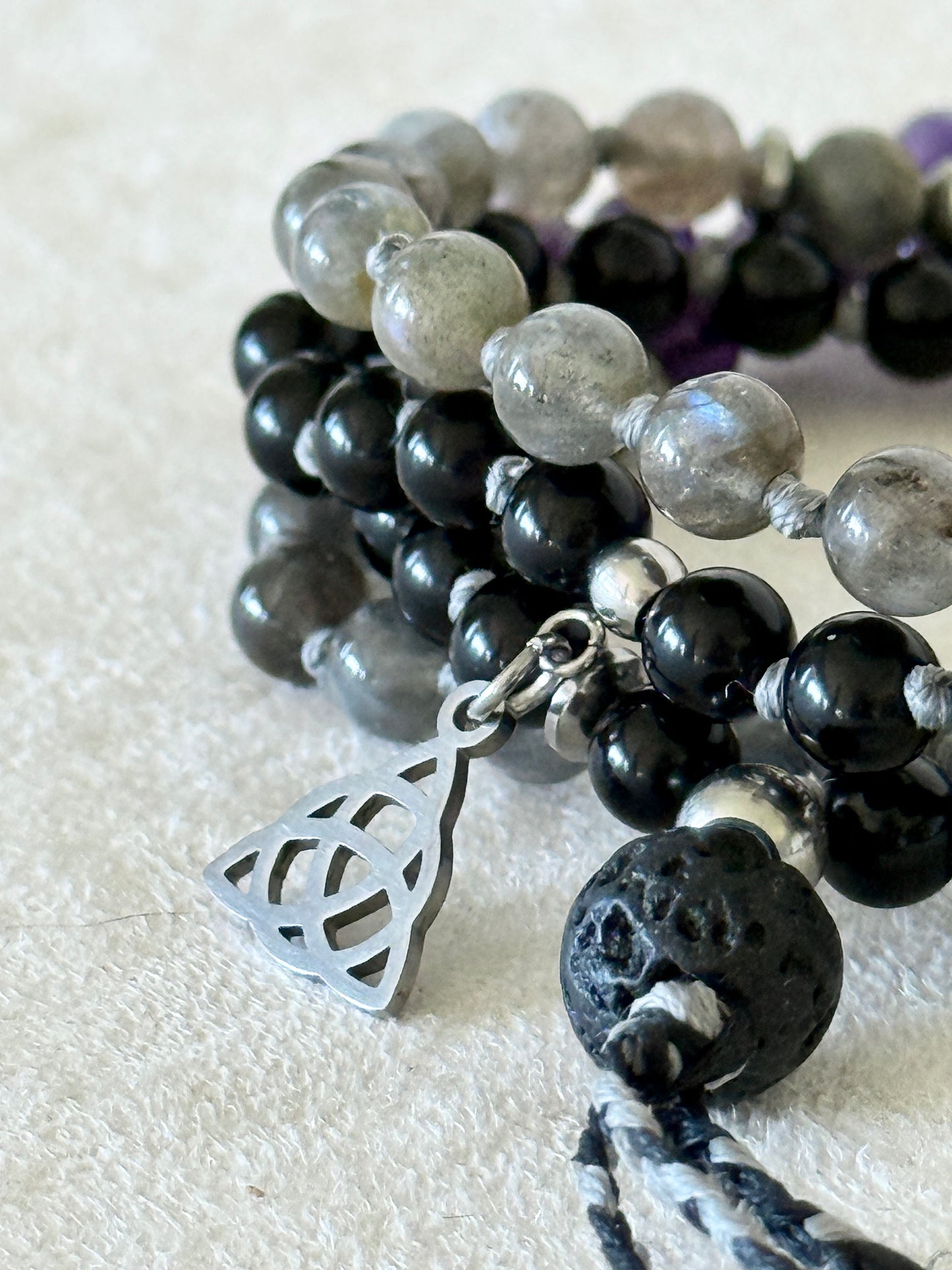 Close-up detail of labradorite and obsidian beads on the Shadow Work Mini Mala, with silver Triquetra charm and lava stone meru bead.