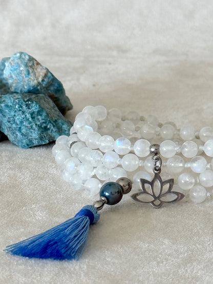Close-up of Hand-knotted Rainbow Moonstone mala necklace with 108 prayer beads, 6 mm natural gemstone beads, Aqua Aura Quartz meru, stainless steel details, small lotus charm, and tassel, created for meditation, breathwork, mantra repetition, mindfulness, and intentional practice.