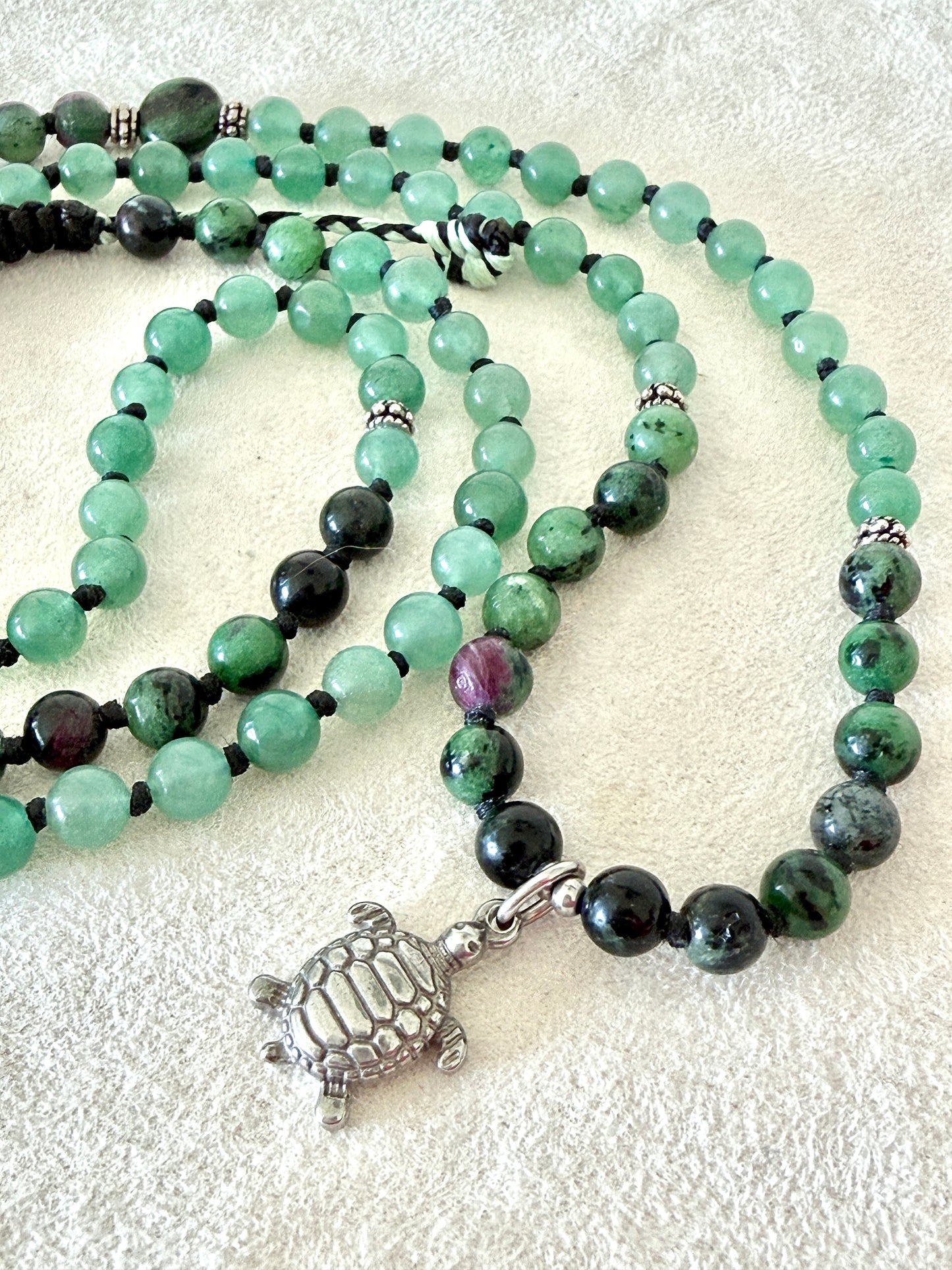 Close-up of Handmade green mala bracelet with natural 6 mm gemstones, stainless steel turtle charm, adjustable macramé closure, and 108 bead mala necklace design for yoga, meditation, gentle growth, protection, and spiritual transformation. 