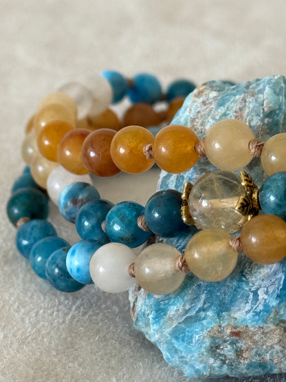 Close-up of The Sun and the sea natural gemstone mala bracelet. Handmade Apatite and Yellow Jade mala bracelet with natural 6 mm gemstones, Citrine guru bead, adjustable macramé closure, and stainless steel details; a 108 bead mala necklace inspired by sea and sun, water and fire, for meditation, yoga, and intention practice.