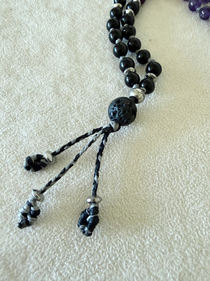 Close-up of the tassel end of the Shadow Work Mini Mala, showing the lava stone meru, engraved Om Mani Padme Hum bead, and black woven tassel with silver caps.