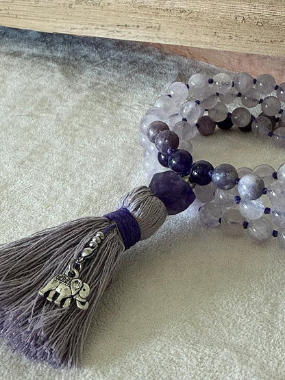 Close up of Purple mala necklace for meditation. Handmade 108 bead mala in netural gemstone 8 mm lavender jade, lepidolite and amethyst with cotton tassel and small elephant charm.