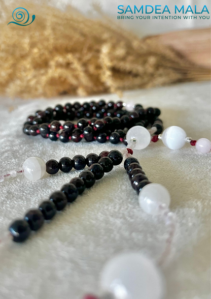 A close-up of a black and white juzu with red beads. Samdea Mala Custom Nichiren Juzu with gemstones.