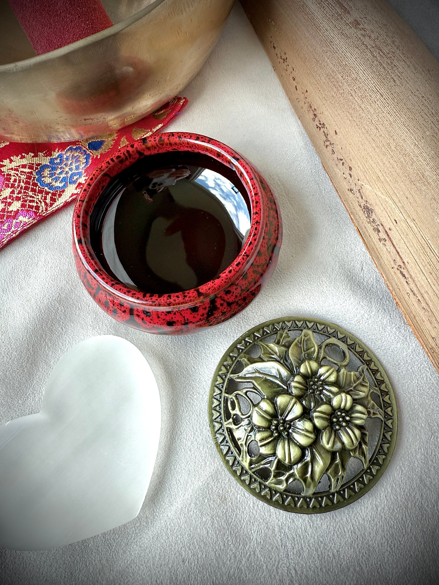 Depp red ceramic container with brass lid placed on a wooden surface as a mindful home sanctuary detail.