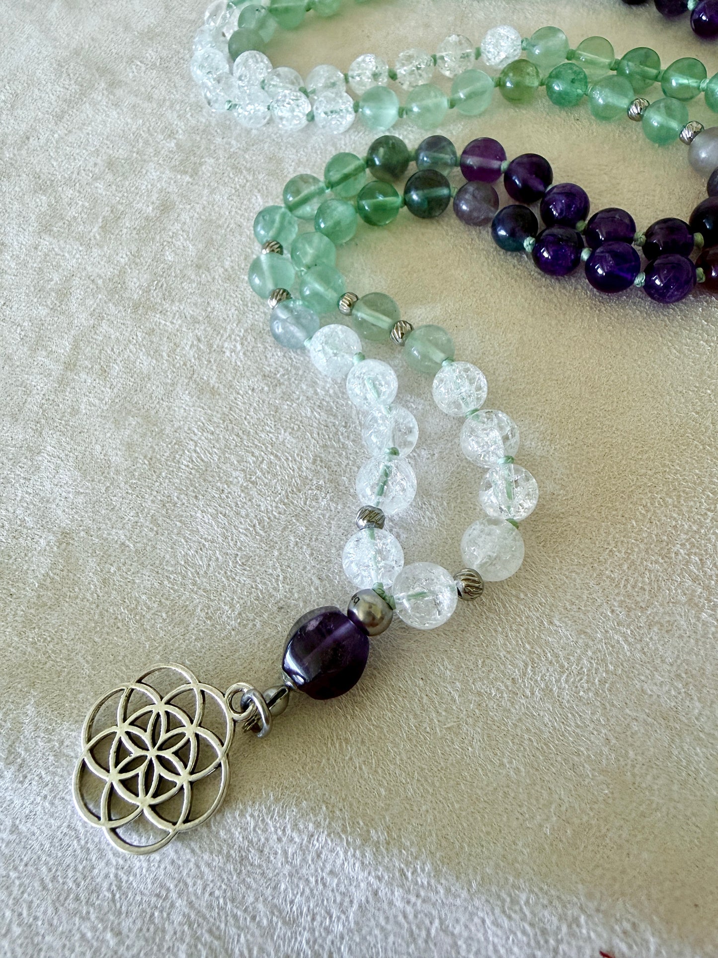 Detail of seed of life on a Natural Green fluorite, amethyst and clear quartz mala necklace for meditation and spiritual practice, Hand-knotted 108 bead mala with natural untreated gemstones and amethyst meru bead