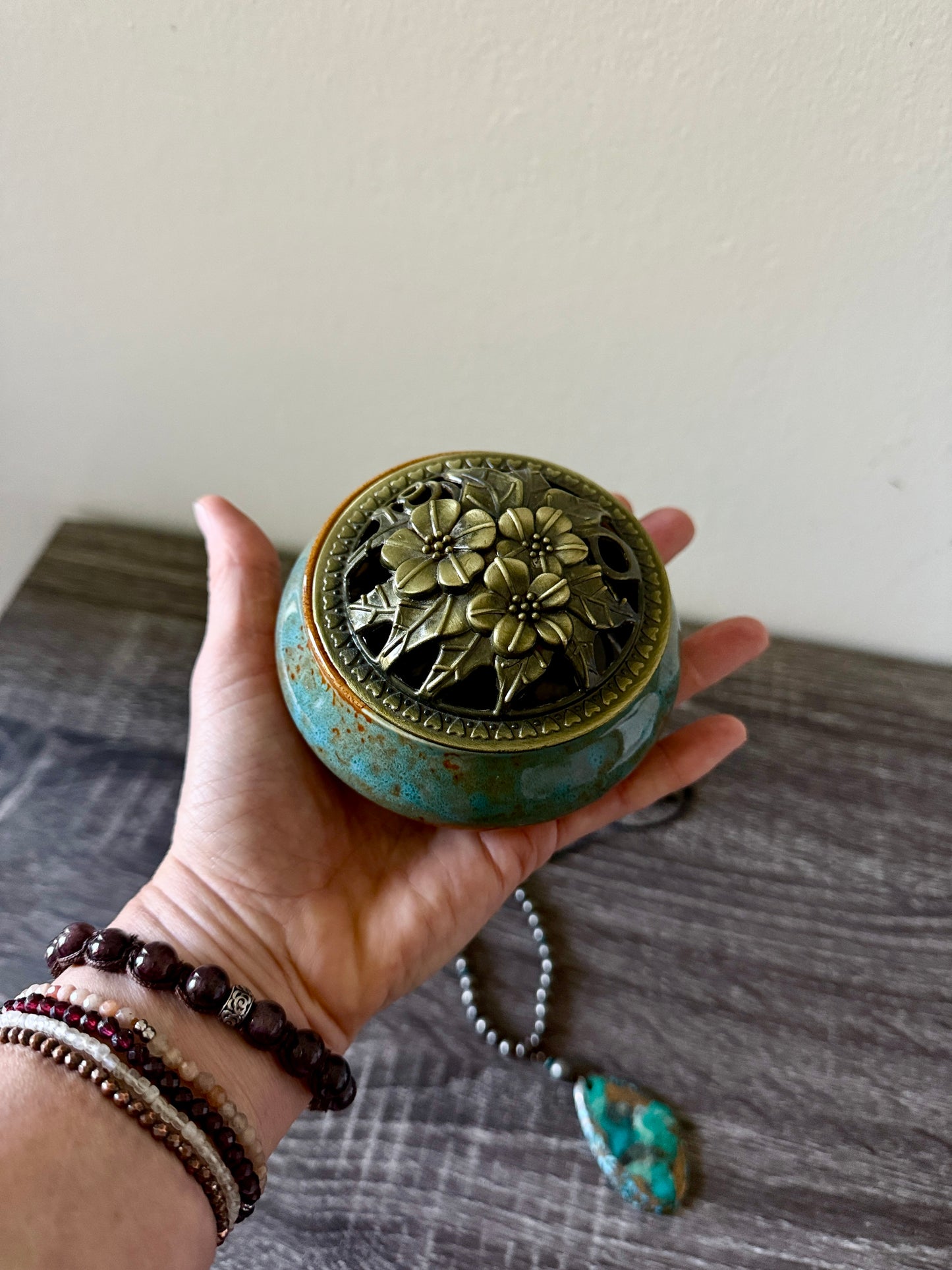 Hand holding home decor accessory. blue ceramic vessel with a polished brass decorative lid, 3 inches diameter, shown as a home decor accessory.