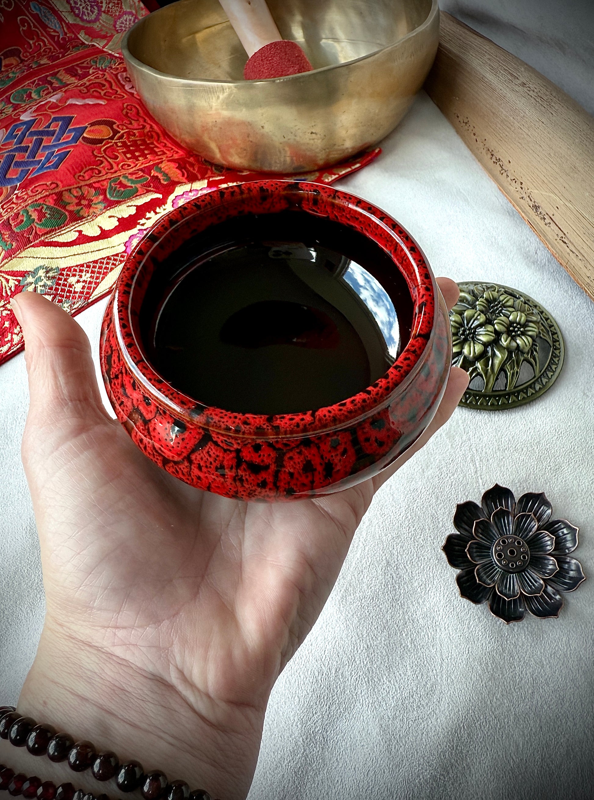 Hand holding Depp red ceramic container with brass lid placed on a wooden surface as a mindful home sanctuary detail.