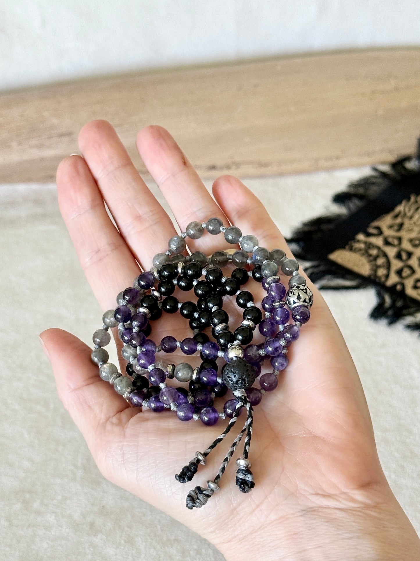 Hand holding the coiled Shadow Work Mini Mala, showing the scale of the 6mm obsidian, amethyst, and labradorite beads