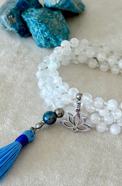 Handmade Rainbow Moonstone mala for meditation with 108 prayer beads, 6 mm natural gemstone beads, Aqua Aura Quartz meru, stainless steel details, small lotus charm, and tassel, created for meditation, breathwork, mantra repetition, mindfulness, and intentional practice. Samdea Mala