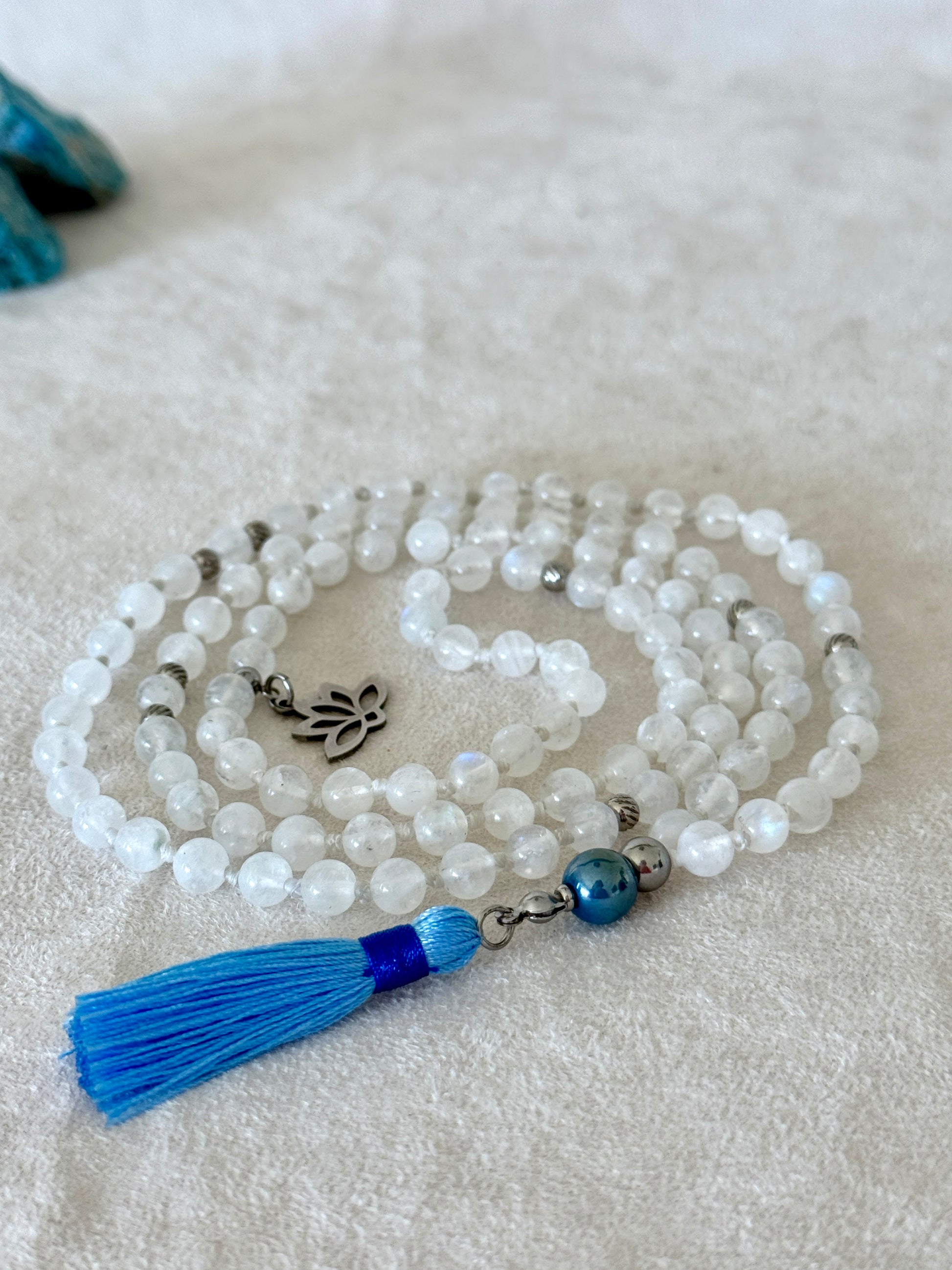 Handmade Rainbow Moonstone mala for meditation with 108 prayer beads, 6 mm natural gemstone beads, Aqua Aura Quartz meru, stainless steel details, small lotus charm, and tassel, created for meditation, breathwork, mantra repetition, mindfulness, and intentional practice. Samdea Mala