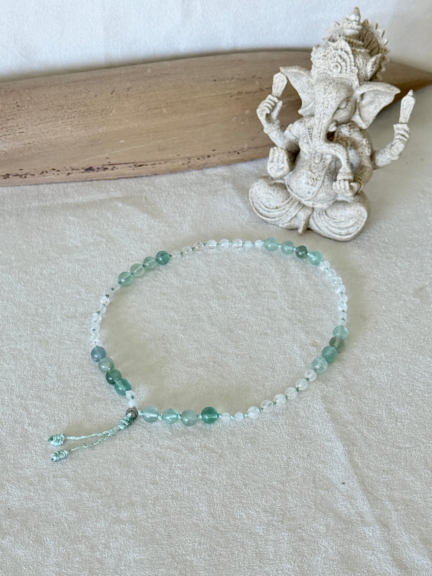 Bracciale mezzo mala Pause Breathing disposto in piano accanto a una statuina di Ganesh, con grani di fluorite, giada bianca e quarzo ialino