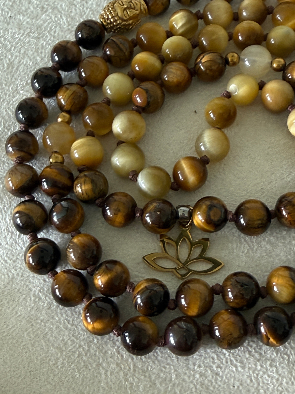 Handmade 108-bead mala necklace with tiger's eye and yellow jade, featuring a Lotus and Buddha charm pendant, designed for grounding, clarity, and centering.