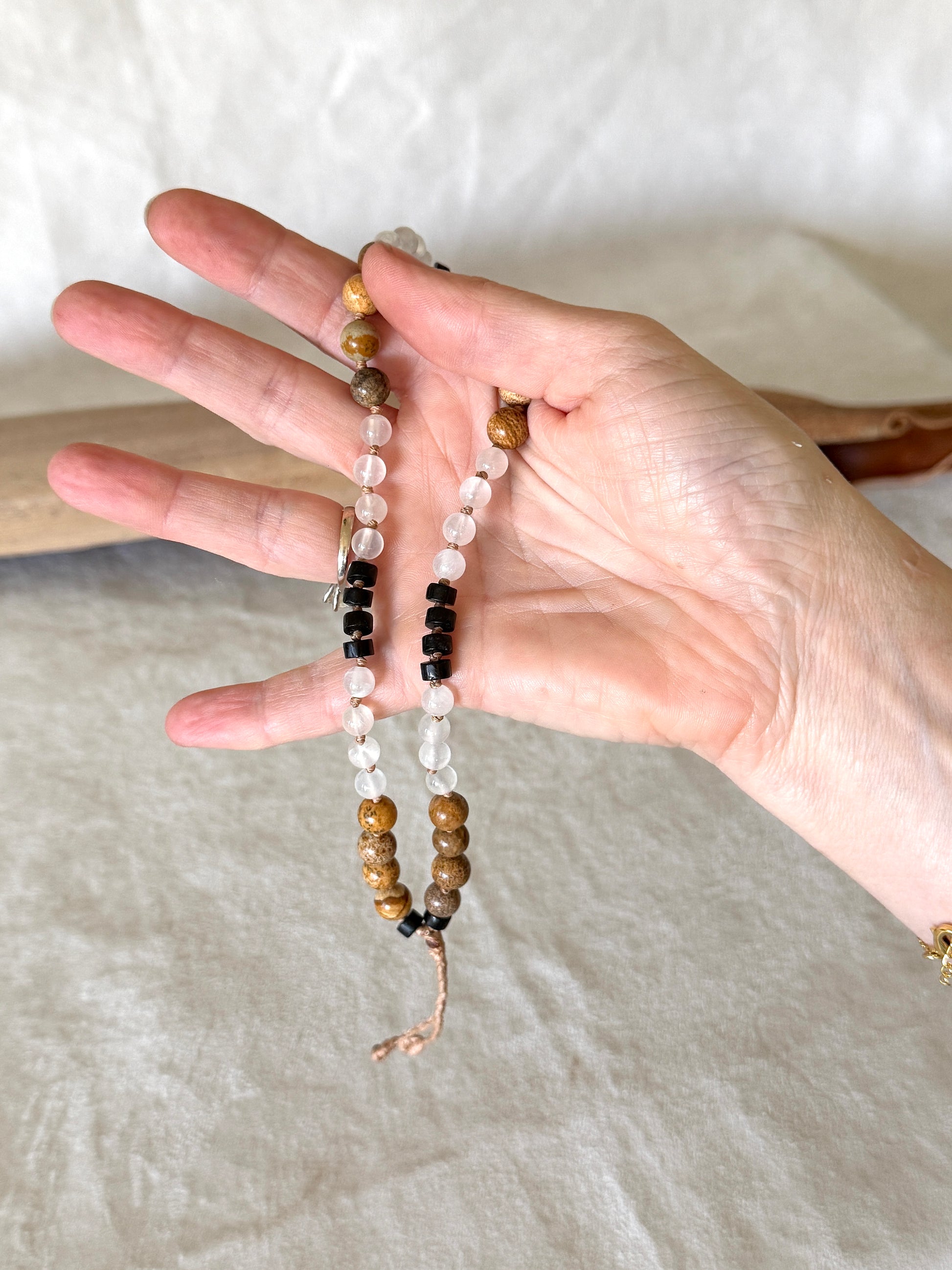 a Hand holding Grounding natural gemstone obsidian, selenite, jasper for breathwork. Mala  bracelet to guide inhale, hold, exhale, and hold during breathing practice.