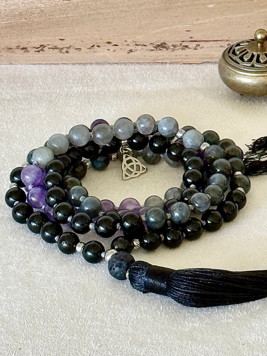 Shadow Work Mala with 108 natural gemstone beads in obsidian, amethyst, dark labradorite and lava stone, finished with a black tassel, Triquetra charm and stainless steel Om Mani Padme Hum mantra bead. Designed as a tactile support for meditation, reflection and shadow work.