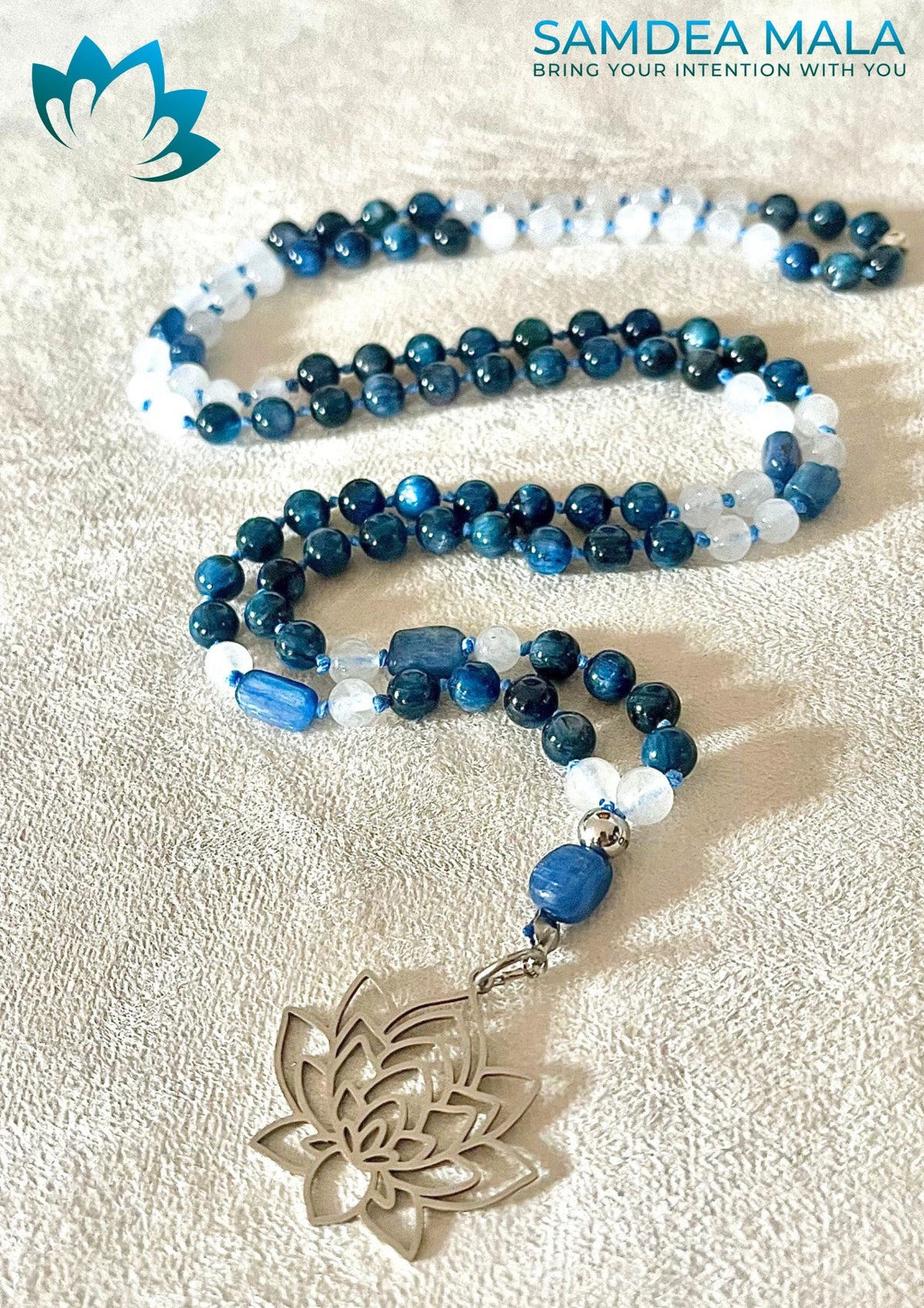 Custom-made kyanite mala with white accent beads and a silver lotus pendant, coiled on a textured cloth