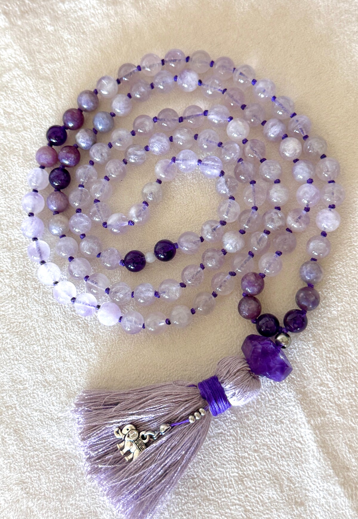 Lavender jade, lepidolite and amethyst 108 bead mala coiled flat, showing the full strand with the amethyst meru bead and silver elephant charm on the tassel