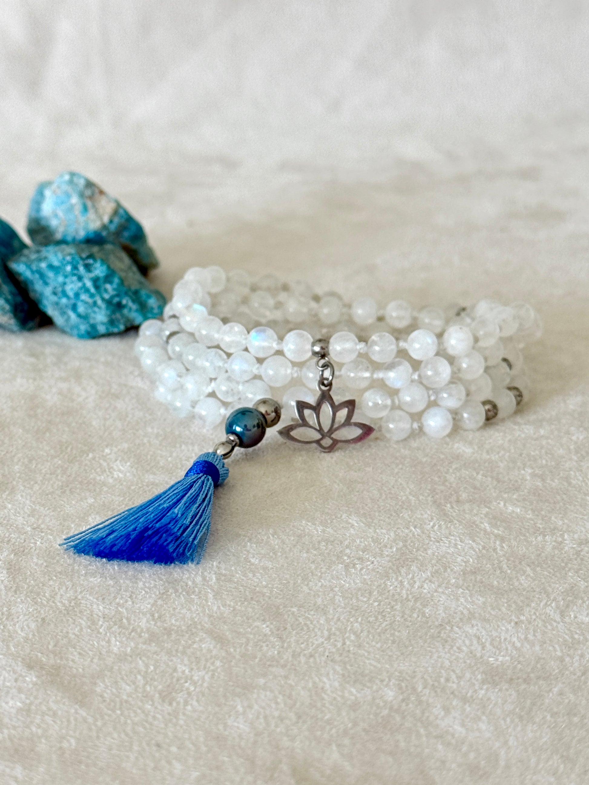 Handmade Rainbow Moonstone mala for meditation with 108 prayer beads, 6 mm natural gemstone beads, Aqua Aura Quartz meru, stainless steel details, small lotus charm, and tassel, created for meditation, breathwork, mantra repetition, mindfulness, and intentional practice. Samdea Mala