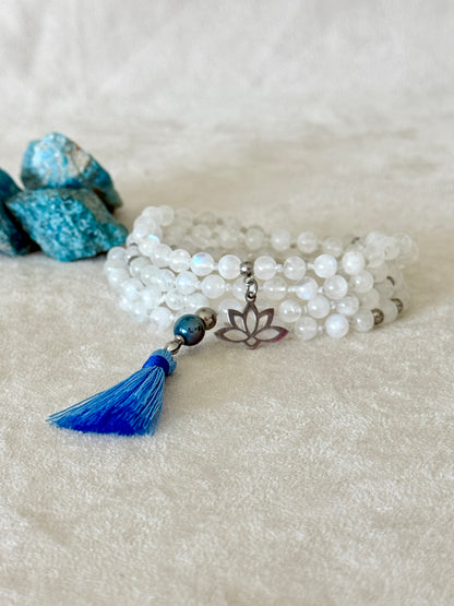 Handmade Rainbow Moonstone mala for meditation with 108 prayer beads, 6 mm natural gemstone beads, Aqua Aura Quartz meru, stainless steel details, small lotus charm, and tassel, created for meditation, breathwork, mantra repetition, mindfulness, and intentional practice. Samdea Mala