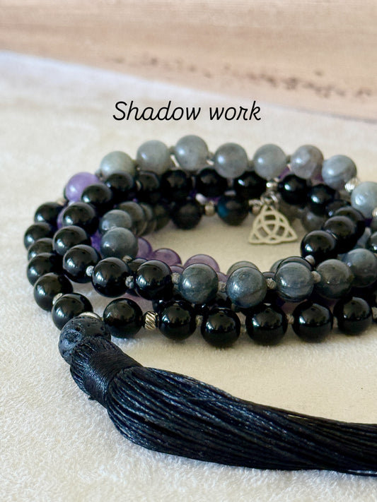 Shadow Work Mala with 108 natural gemstone beads in obsidian, amethyst, dark labradorite and lava stone, finished with a black tassel, Triquetra charm and stainless steel Om Mani Padme Hum mantra bead. Designed as a tactile support for meditation, reflection and shadow work.