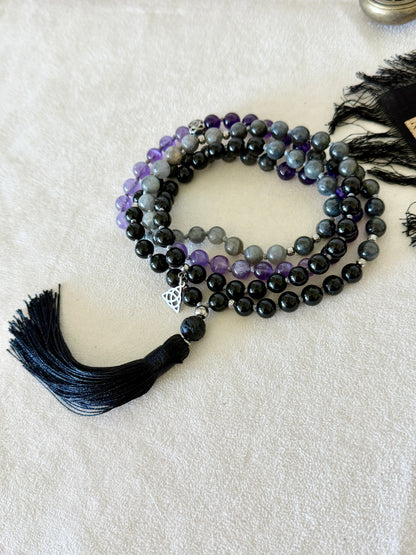 Shadow Work Mala with 108 natural gemstone beads in obsidian, amethyst, dark labradorite and lava stone, finished with a black tassel, Triquetra charm and stainless steel Om Mani Padme Hum mantra bead. Designed as a tactile support for meditation, reflection and shadow work.