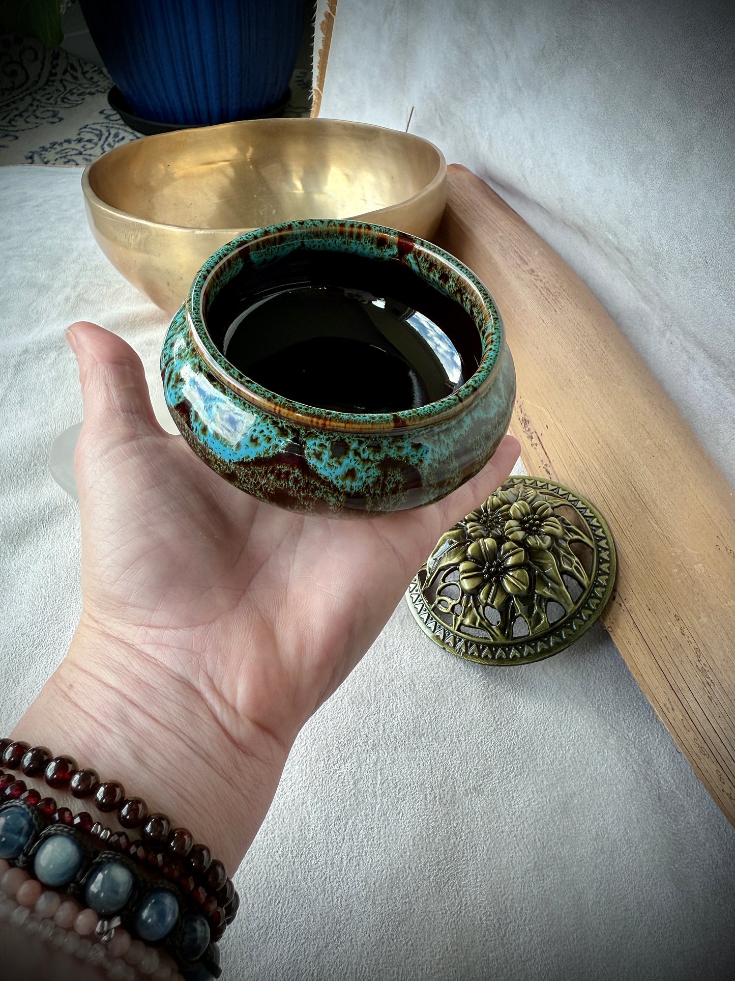 Small round ceramic bowl in deep blue glaze with a removable golden metallic lid, artisanal tabletop decor. On hand