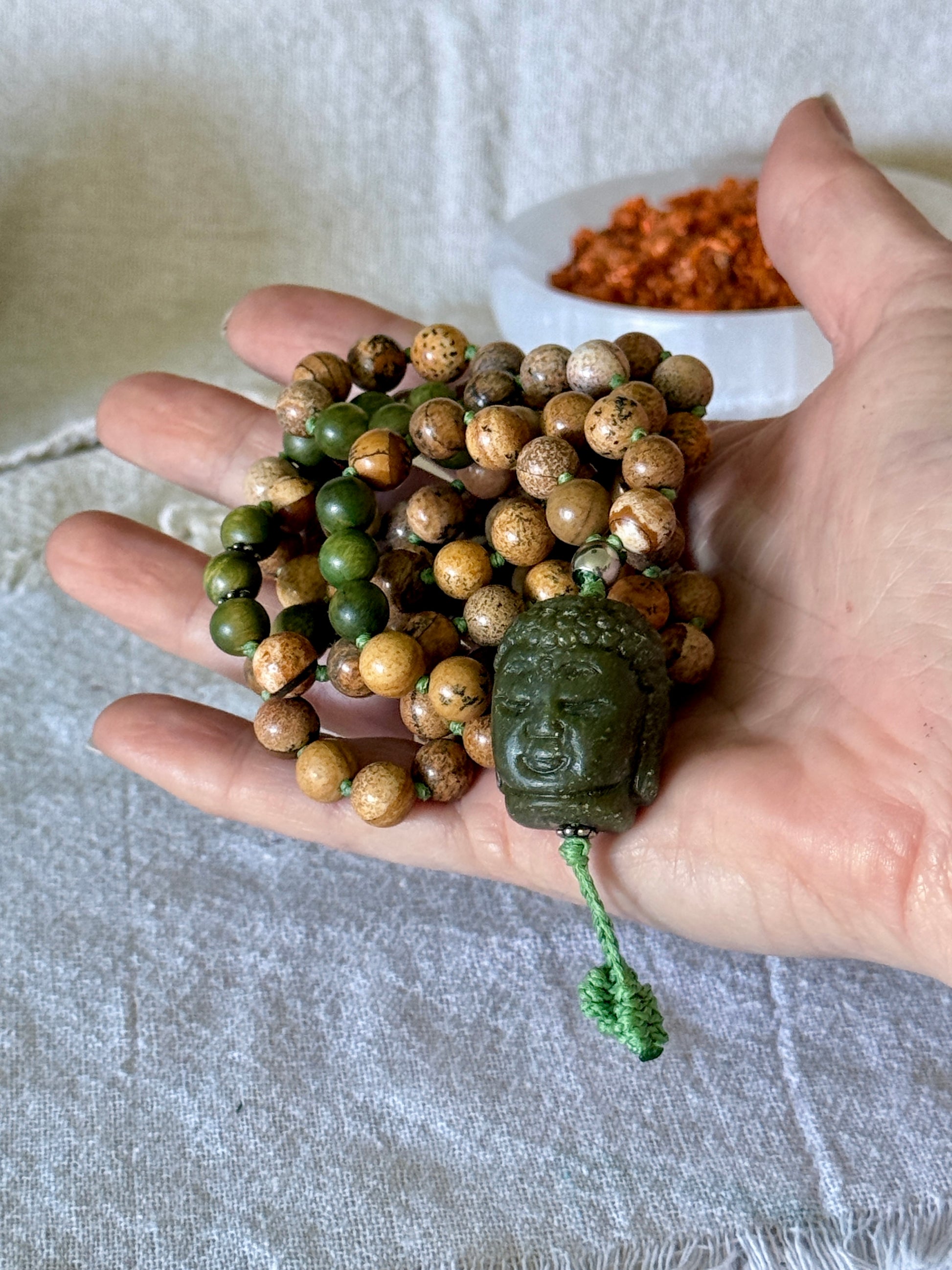 Genuine sandalwood mala necklace with 108 hand-knotted beads, earthy sand jasper, and Jade Buddha meru bead on a hand
