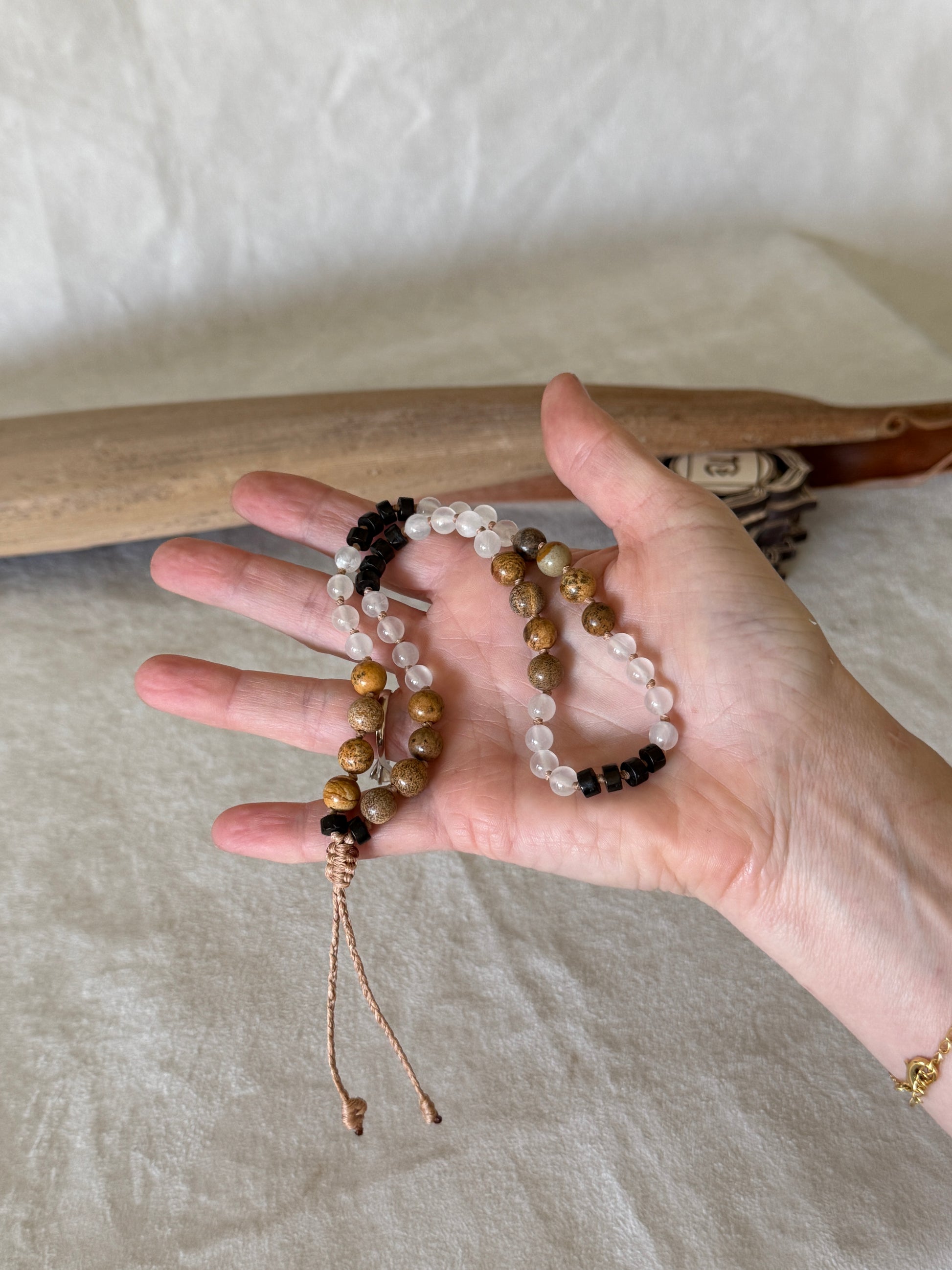 a Hand holding Grounding natural gemstone obsidian, selenite, jasper for breathwork. Mala  bracelet to guide inhale, hold, exhale, and hold during breathingpractice.