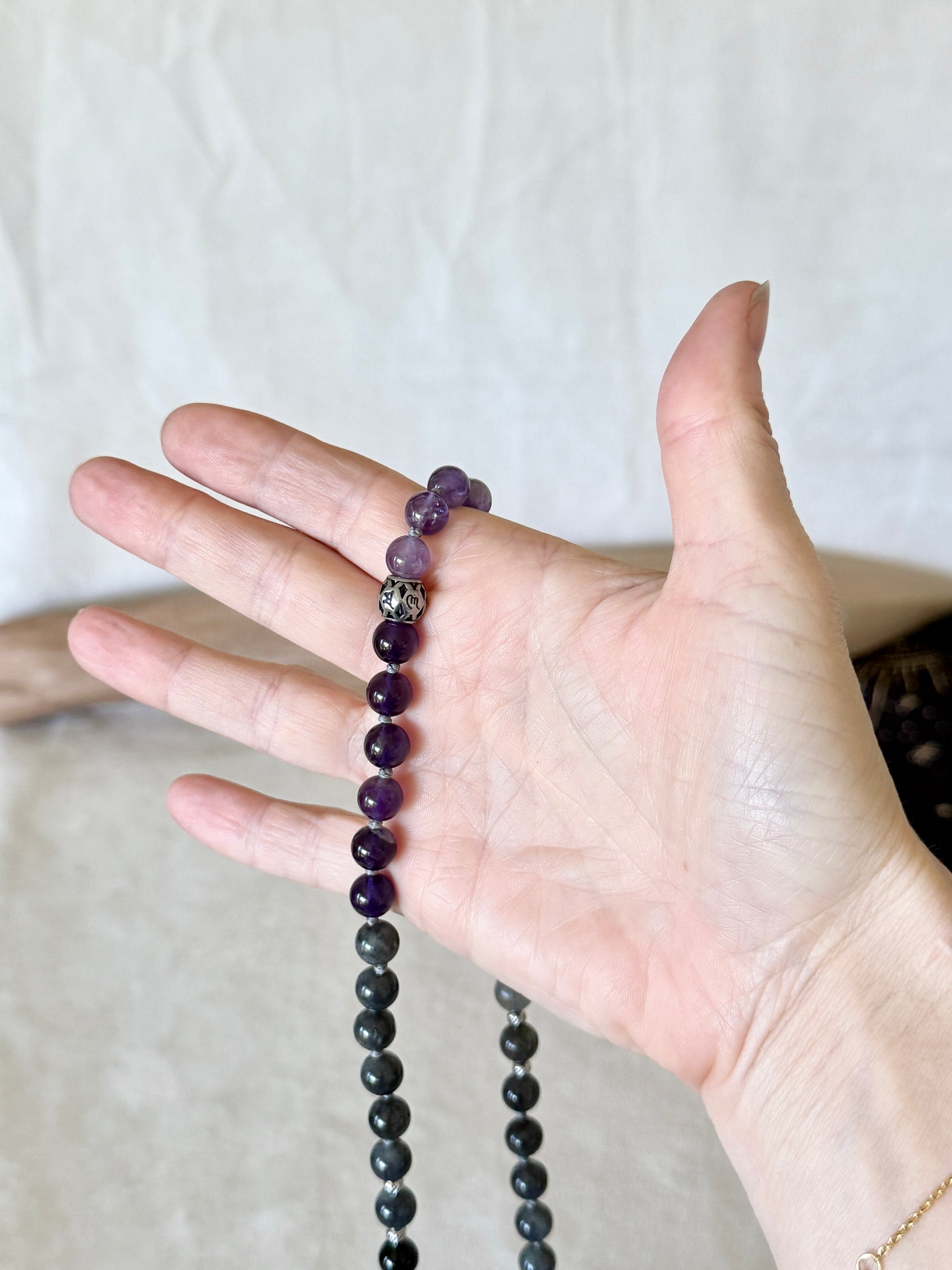 a hand holding the Shadow Work Mala beads in obsidian, amethyst and dark labradorite