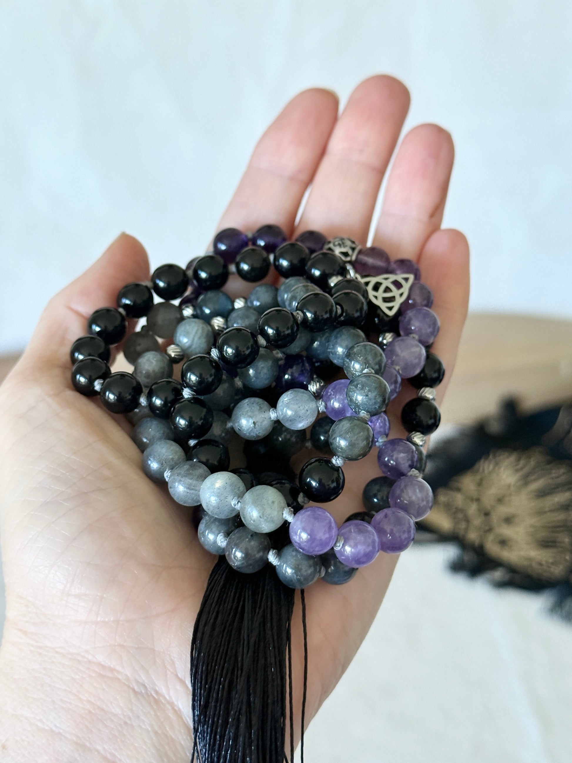 a hand holding the Shadow Work Mala beads in obsidian, amethyst and dark labradorite