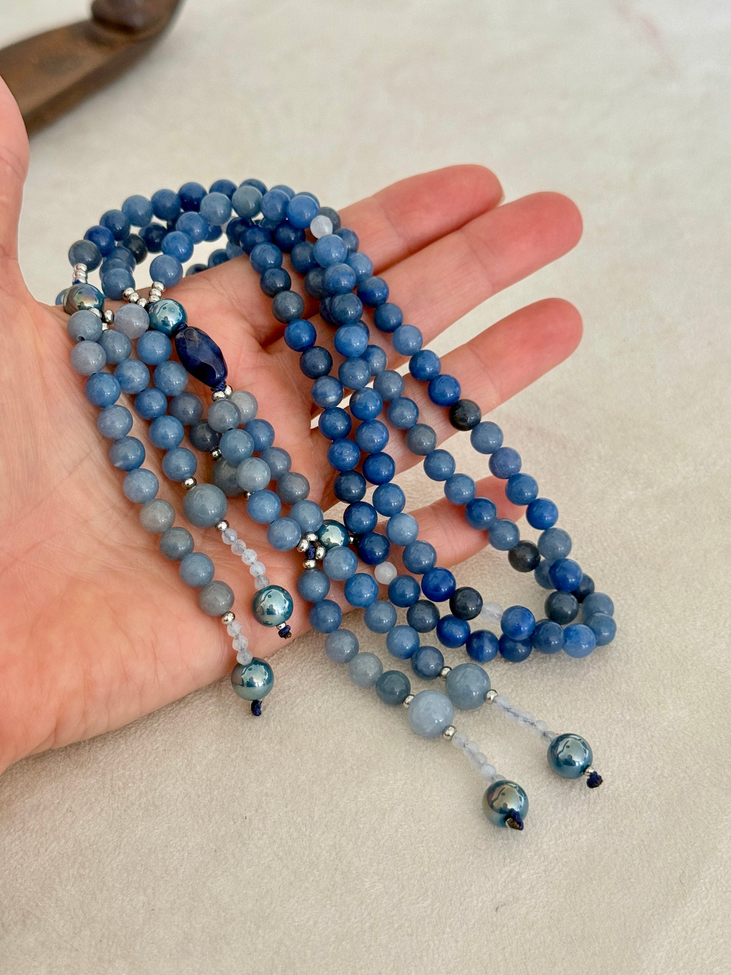 blue SGI Buddhist prayer beads on hand, handmade Japanese Nichiren juzu for Daimoku chanting, Nam Myoho Renge Kyo meditation, with blue aventurine, Burmese white jade Bodhisattva, aqua aura accents, and lapis lazuli details.