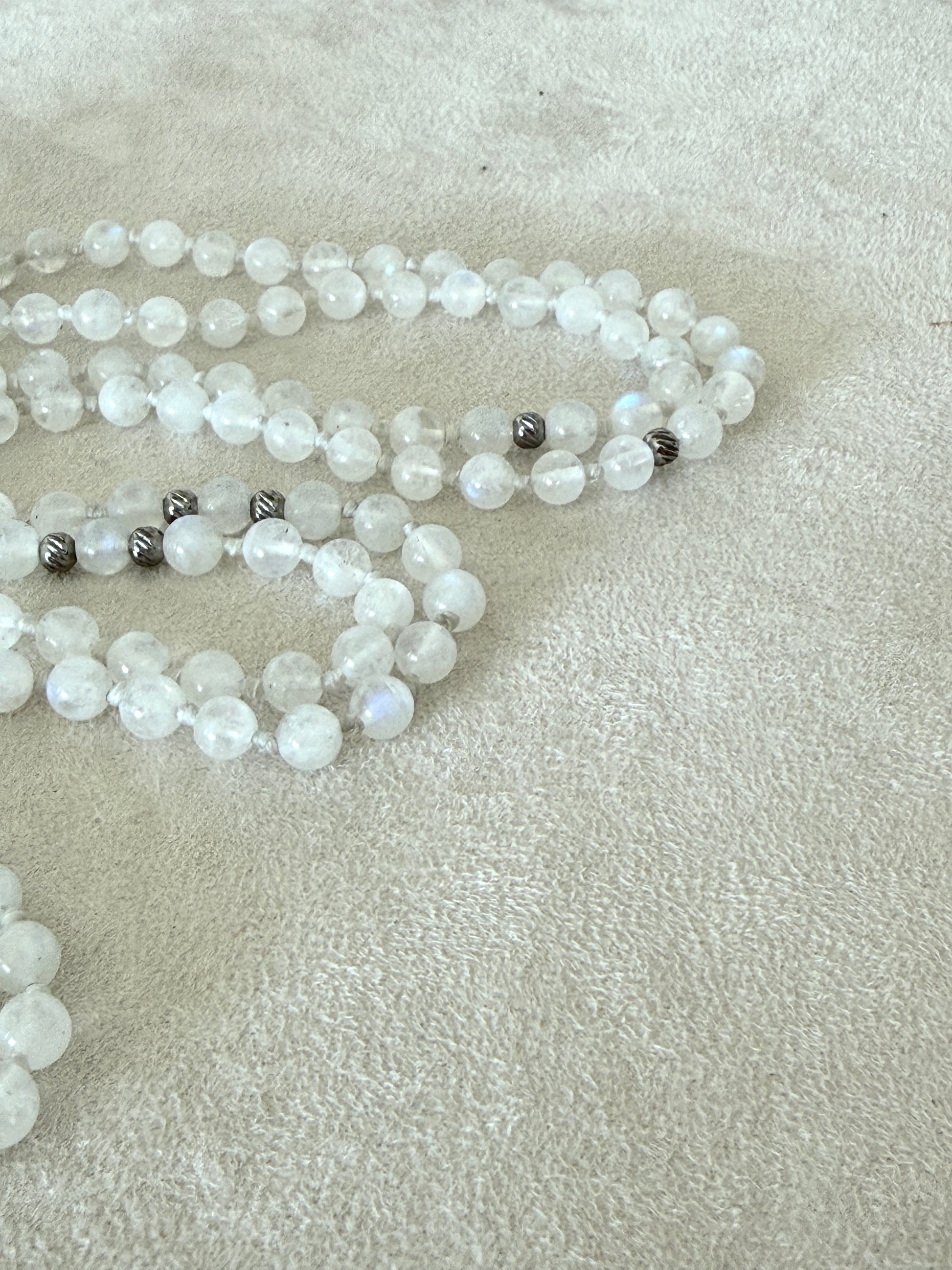 Detail of a  Handmade Rainbow Moonstone mala for meditation with 108 prayer beads, 6 mm natural gemstone beads, Aqua Aura Quartz meru, stainless steel details, small lotus charm, and tassel, created for meditation, breathwork, mantra repetition, mindfulness, and intentional practice. Samdea Mala