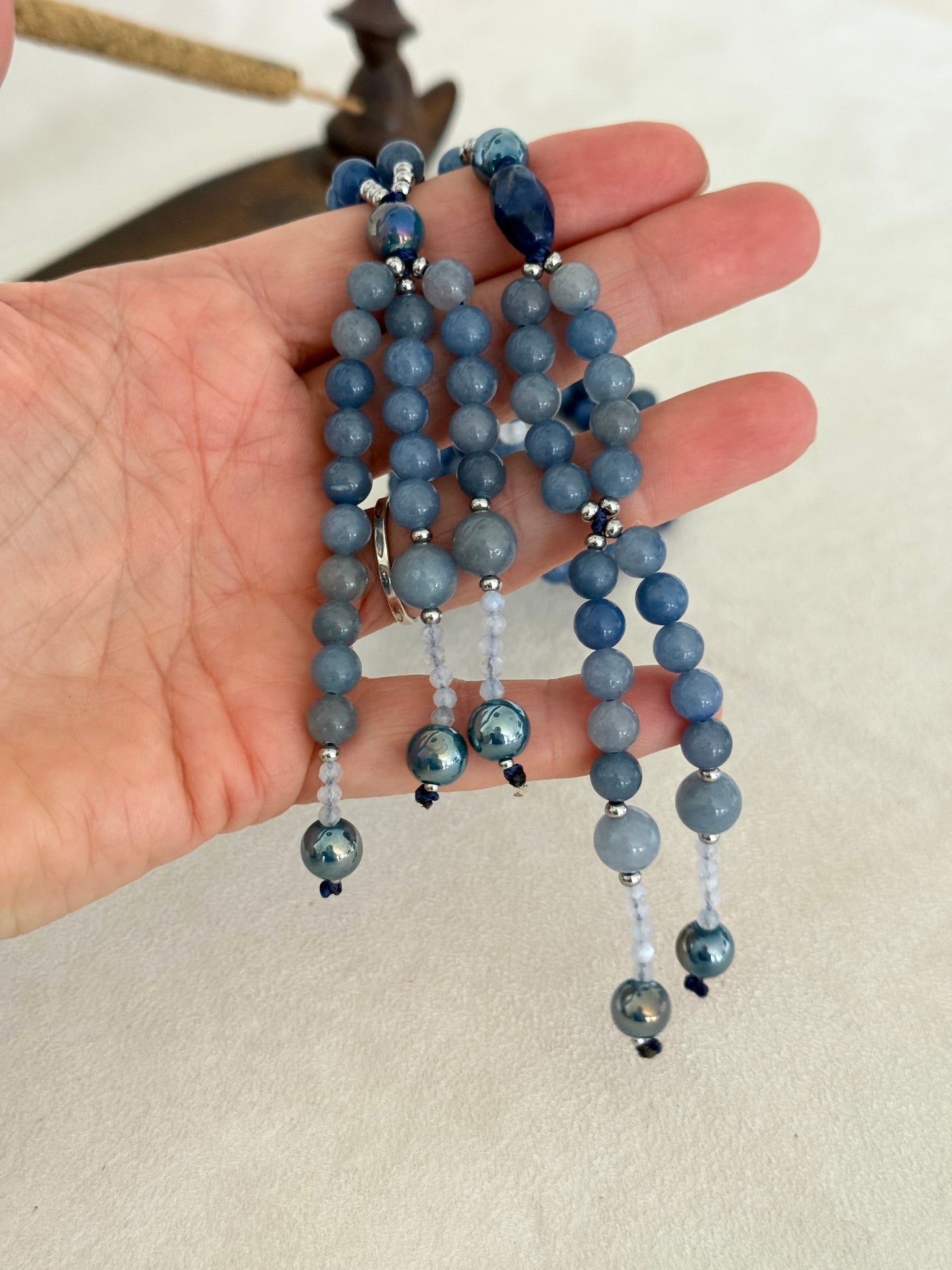 detail of blue SGI Buddhist prayer beads on hand, handmade Japanese Nichiren juzu for Daimoku chanting, Nam Myoho Renge Kyo meditation, with blue aventurine, Burmese white jade Bodhisattva, aqua aura accents, and lapis lazuli details.