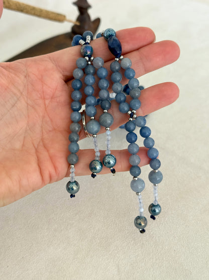 detail of blue SGI Buddhist prayer beads on hand, handmade Japanese Nichiren juzu for Daimoku chanting, Nam Myoho Renge Kyo meditation, with blue aventurine, Burmese white jade Bodhisattva, aqua aura accents, and lapis lazuli details.