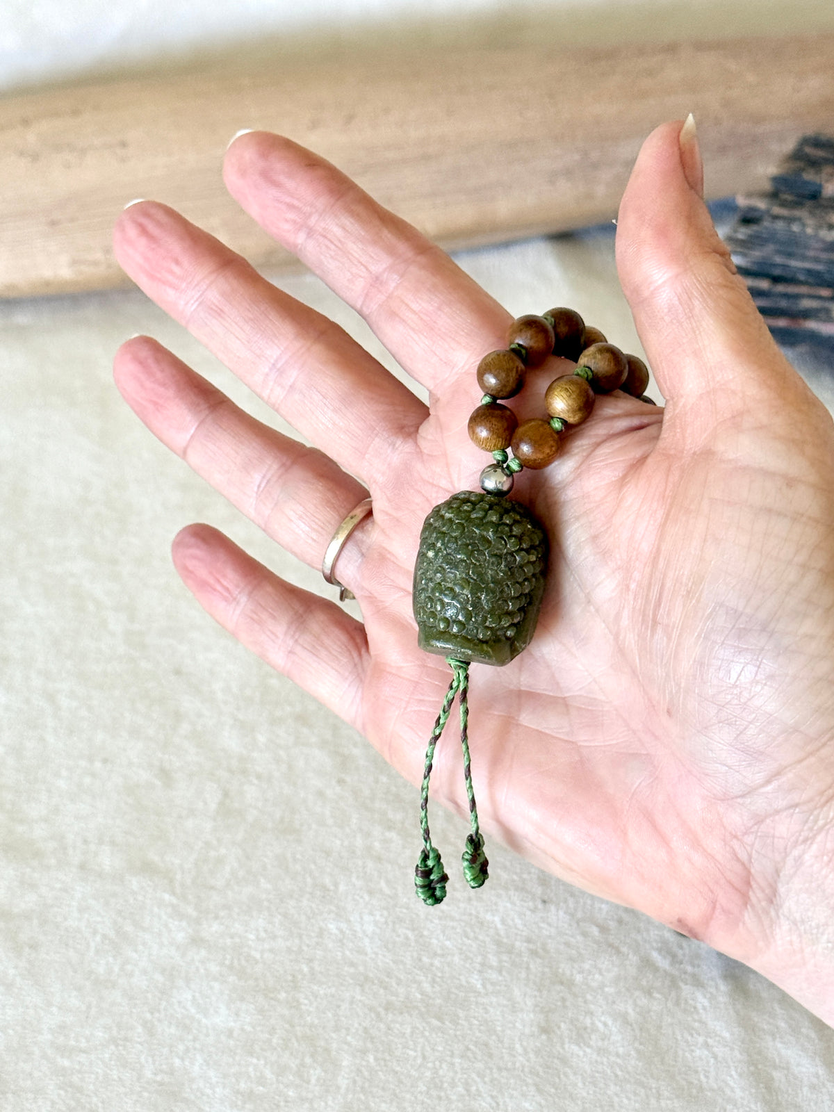 Close-up of the hand-carved jade Buddha pendant on the sandalwood and Indian agate mala, back view